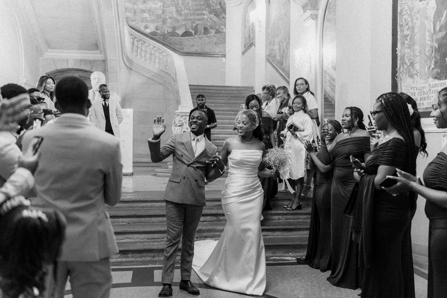 Black and white photo of wedding guests dancing and celebrating in a grand ballroom setting.