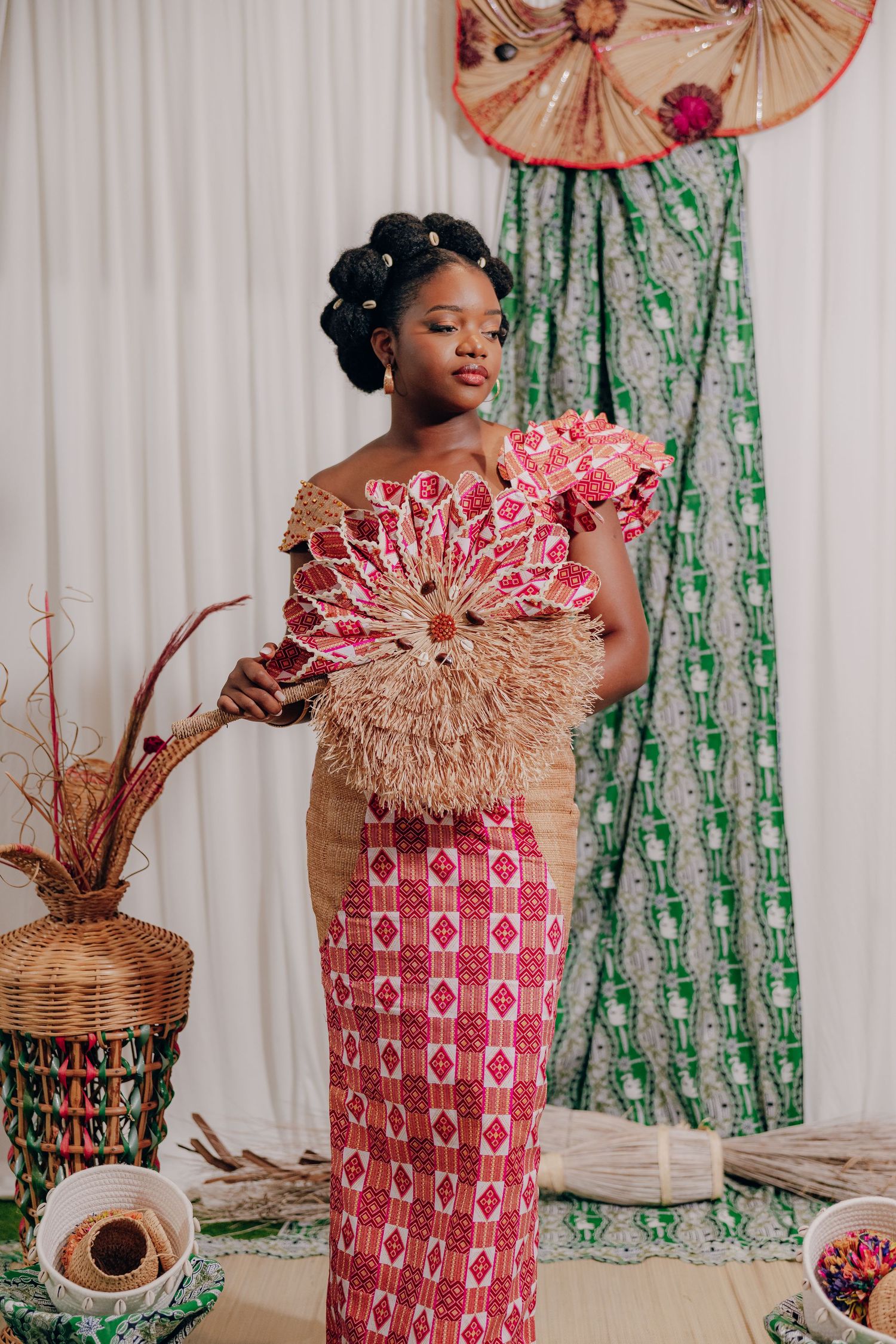 Decorative fans and traditional African prints adorn a wedding celebration space with white curtain backdrop.