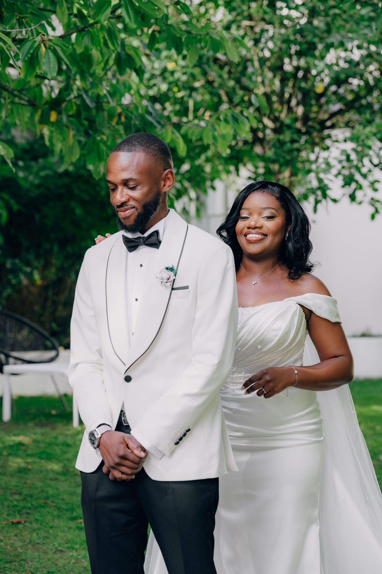 A couple shares a joyful moment in their elegant wedding attire featuring a white tuxedo jacket and off-shoulder gown.