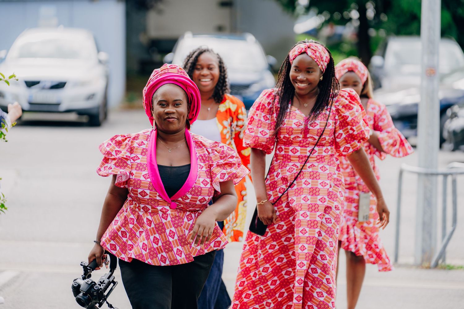 Two people in matching pink and white floral dresses walk together outdoors on a sunny day.