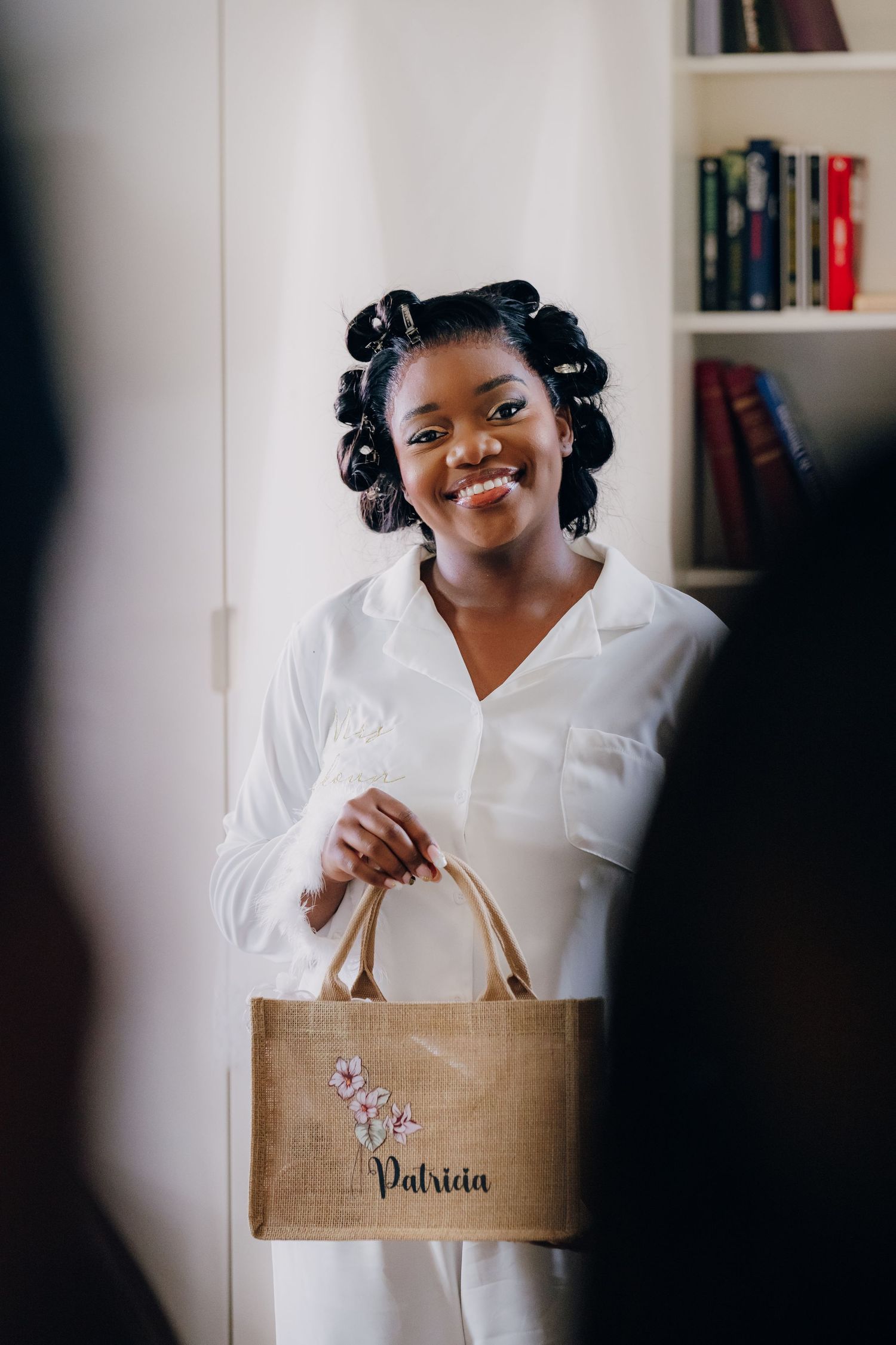 A person wearing a white blouse holds up a natural jute tote bag while smiling.