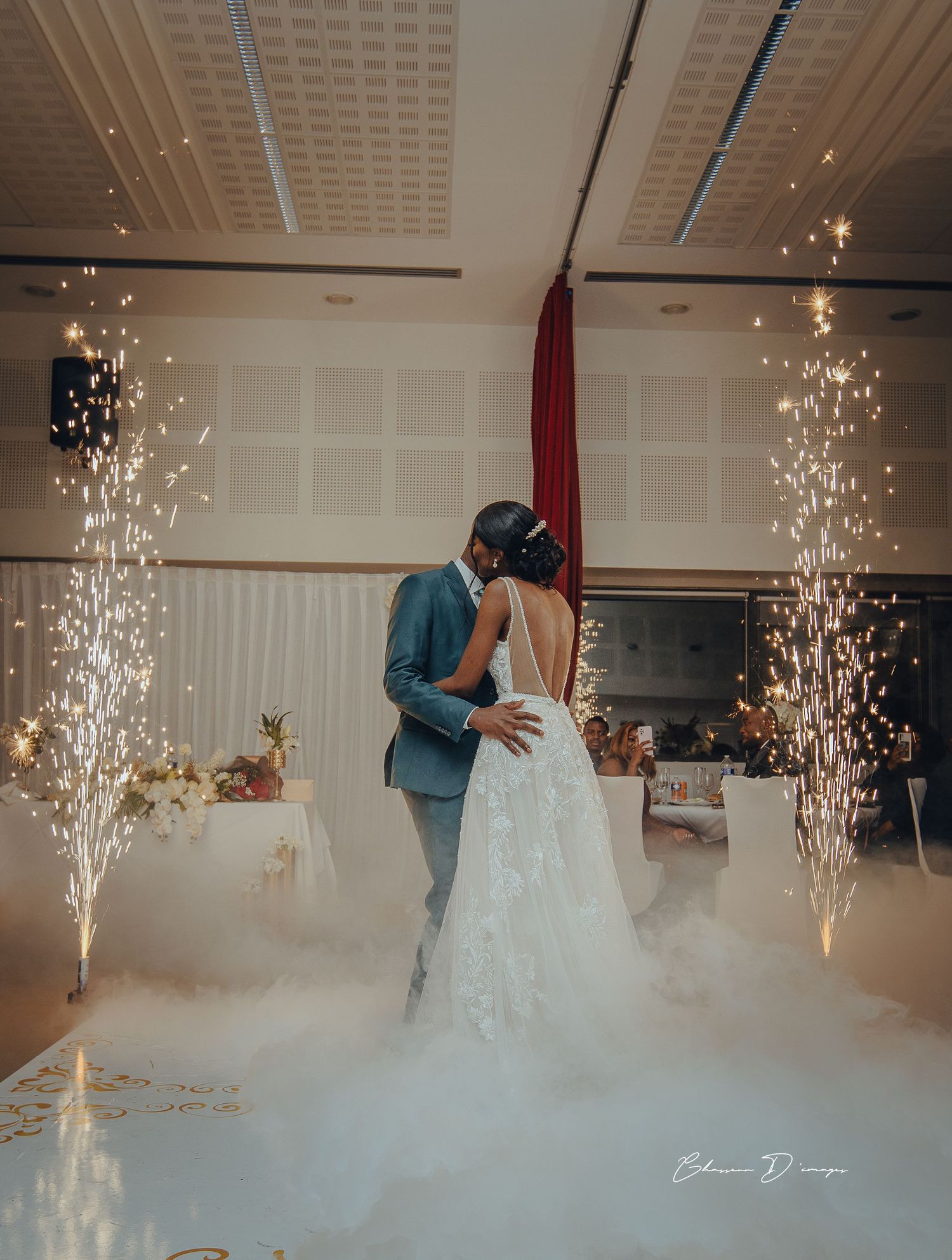 Newlyweds share intimate first dance amid fog and sparklers in an elegantly decorated wedding reception hall.