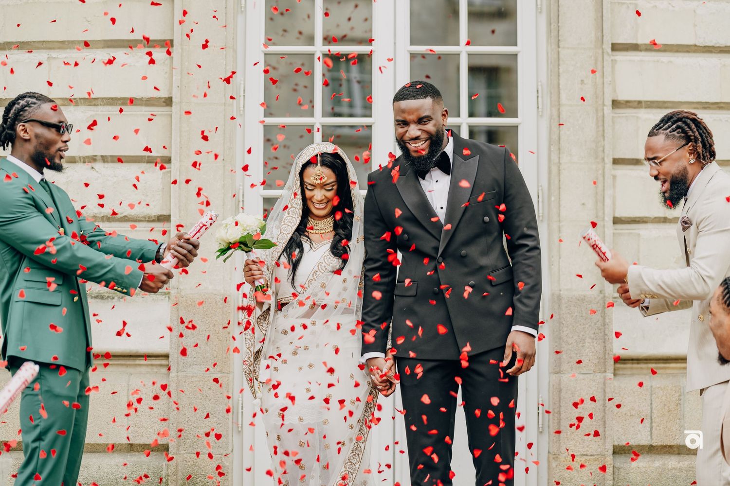 Celebrating newlyweds showered with red confetti outside a classical building.