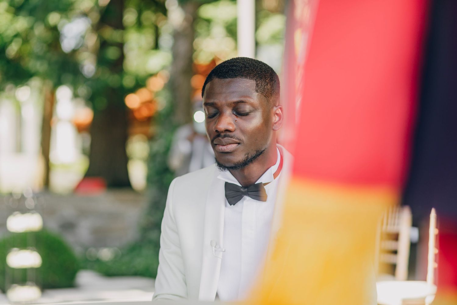 A person in a dark suit and bow tie smiles while sitting at an elegant table setting with wine glasses.