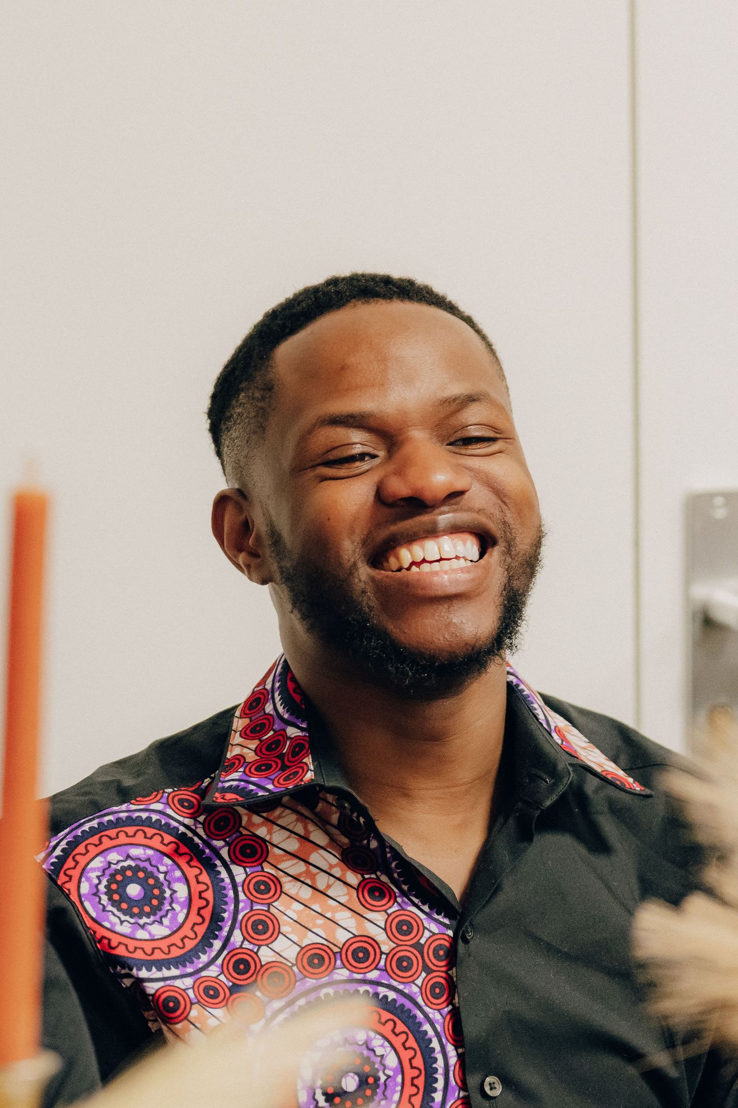 Person wearing patterned shirt smiling brightly against light background.