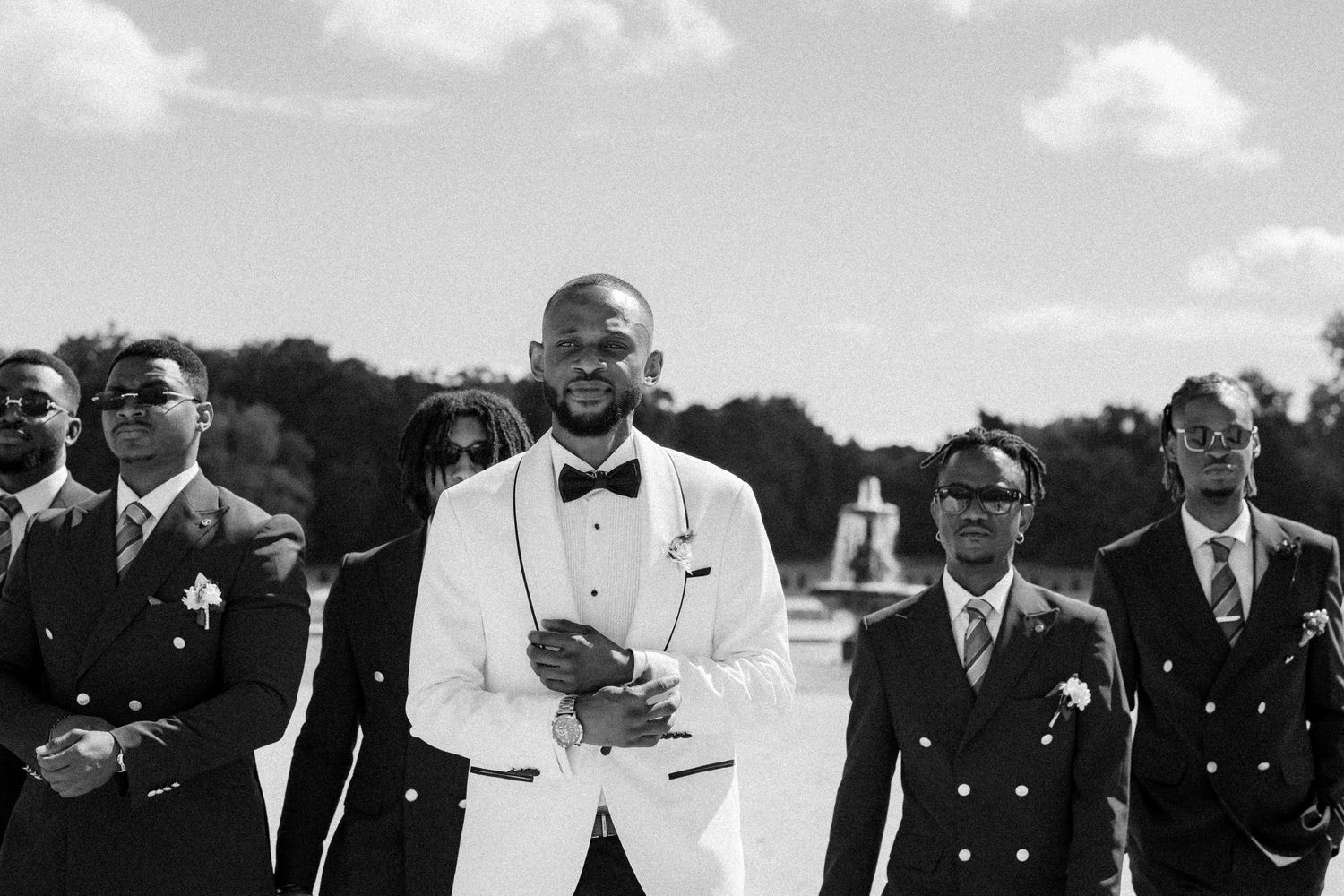 Black and white photo of groomsmen laughing together during outdoor wedding celebration.