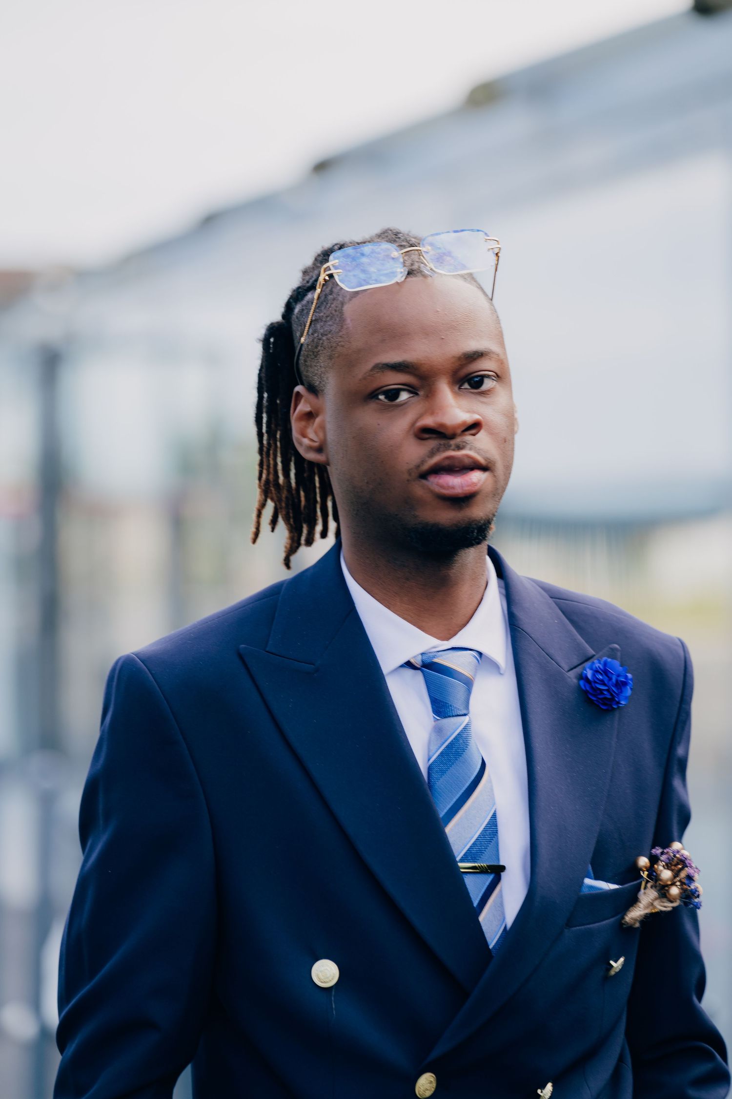 A formal event attendee wearing a navy suit with a blue tie and boutonniere against a light background.