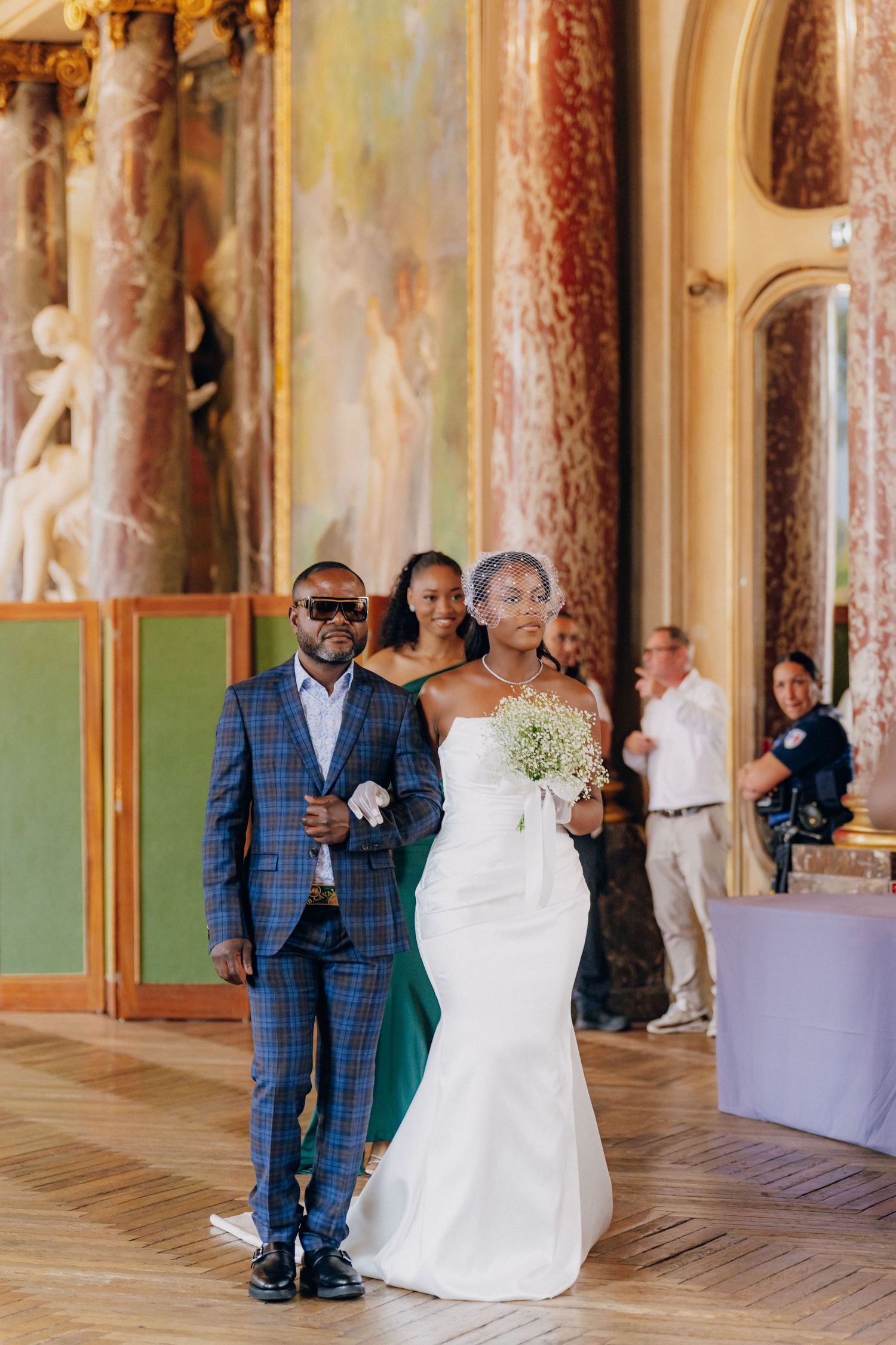 A bride and groom share a tender moment during their first dance in an elegant ballroom with ornate decor.