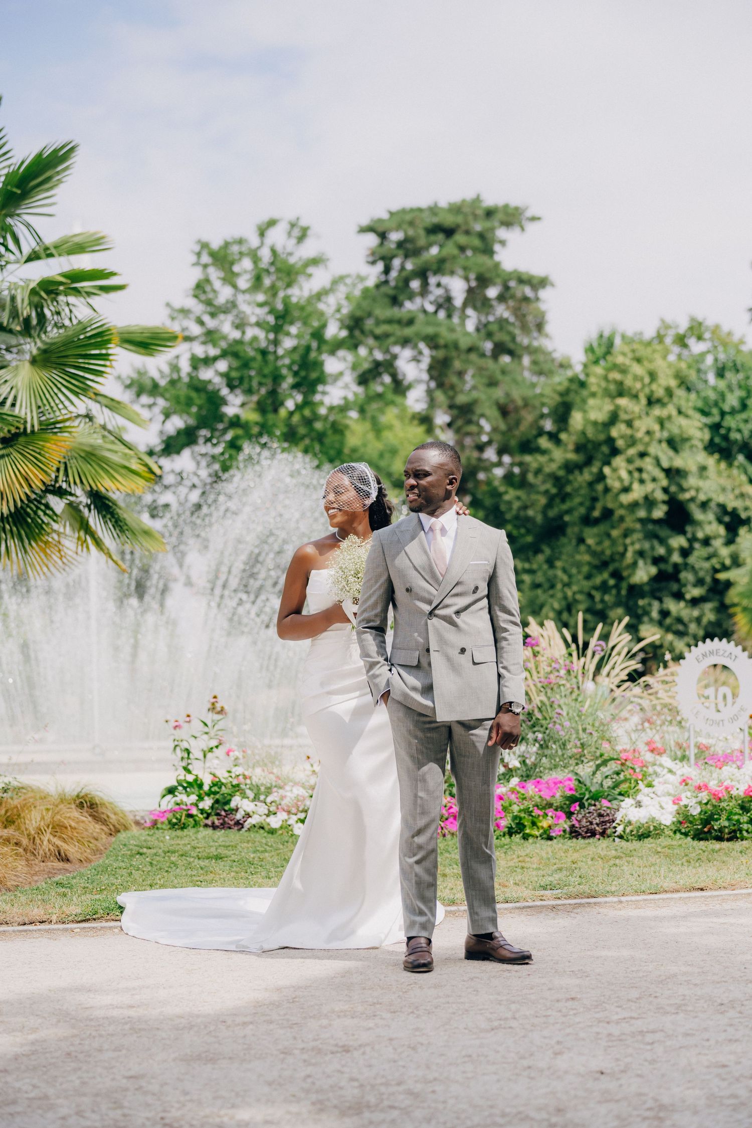 A romantic wedding photo of a couple posing in front of a garden fountain and blooming flowers on their special day.