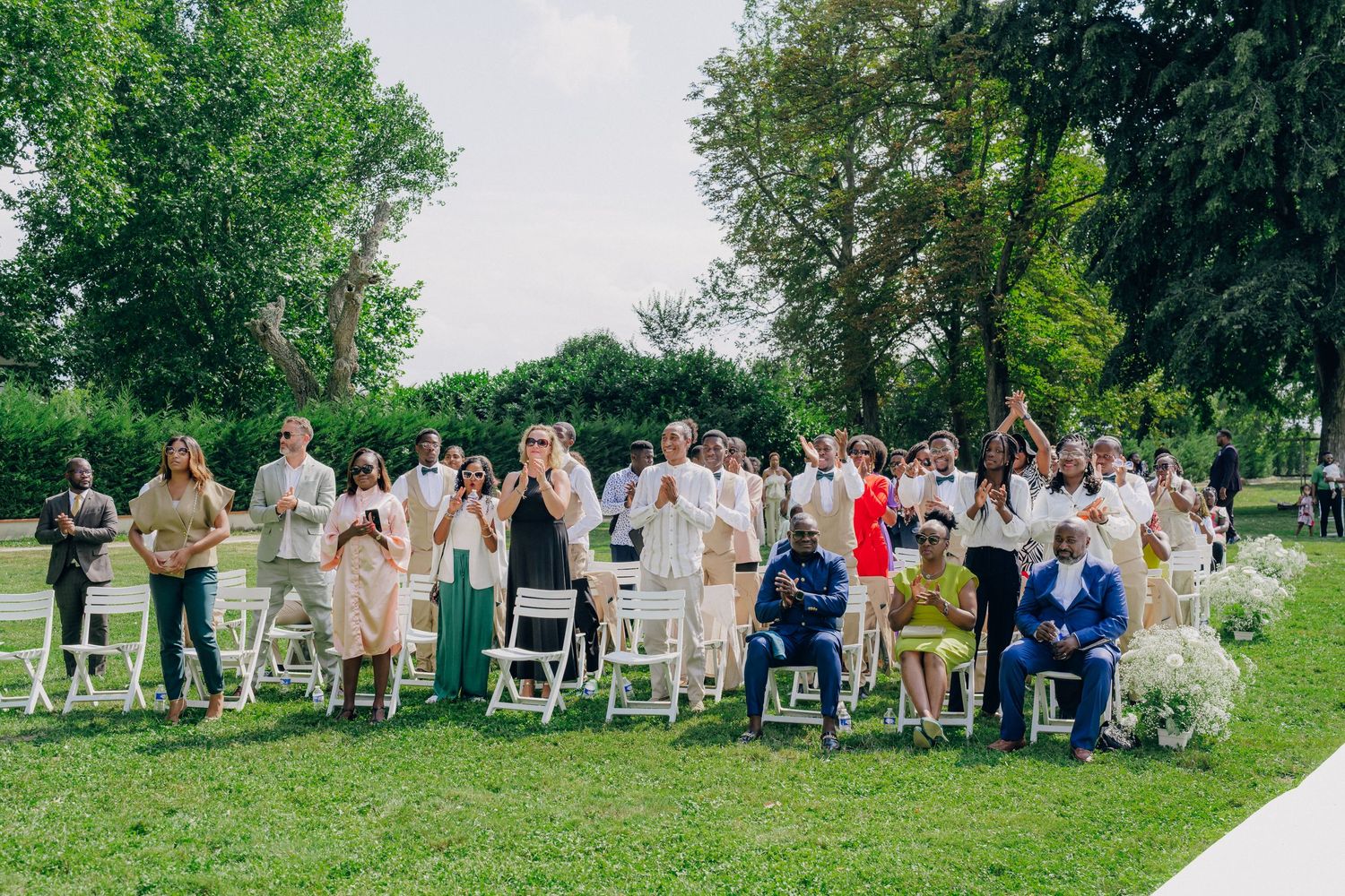 Wedding guests seated in white chairs on a lush green lawn for an outdoor ceremony.