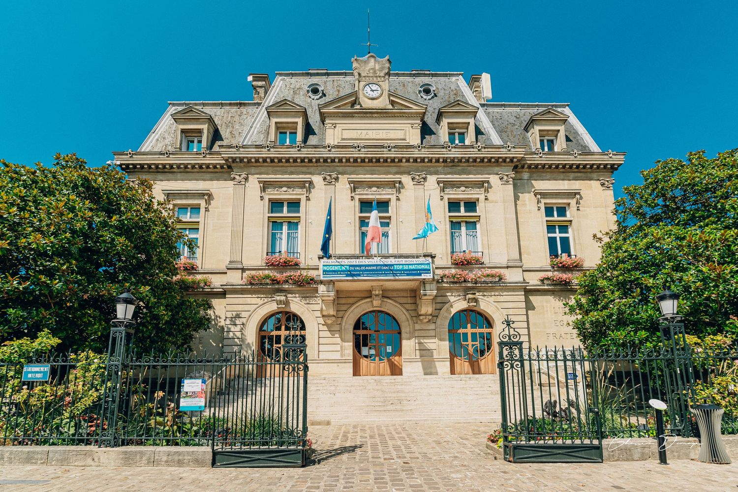 Elegant French-style mansion with ornate architecture and iron gates under bright blue sky.