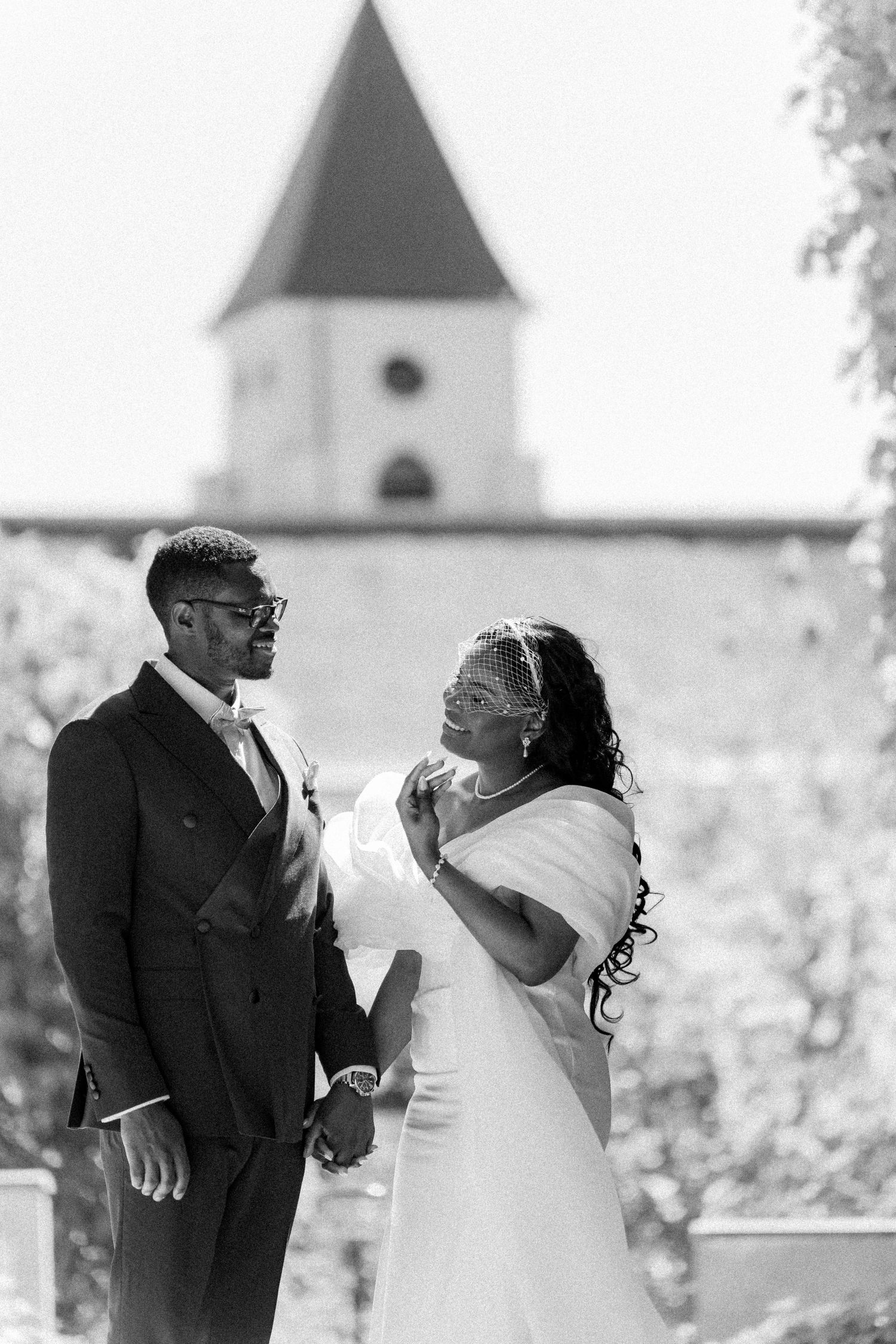 A black and white wedding photo showing a joyful couple sharing a moment together with a church steeple in the background.
