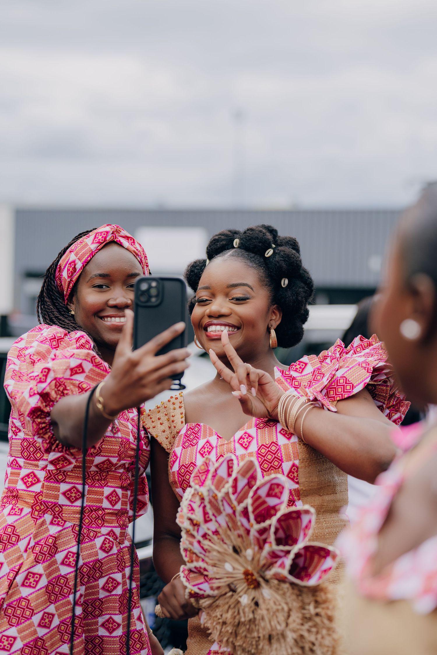 Friends taking selfies and laughing together while wearing vibrant pink and red patterned traditional attire.