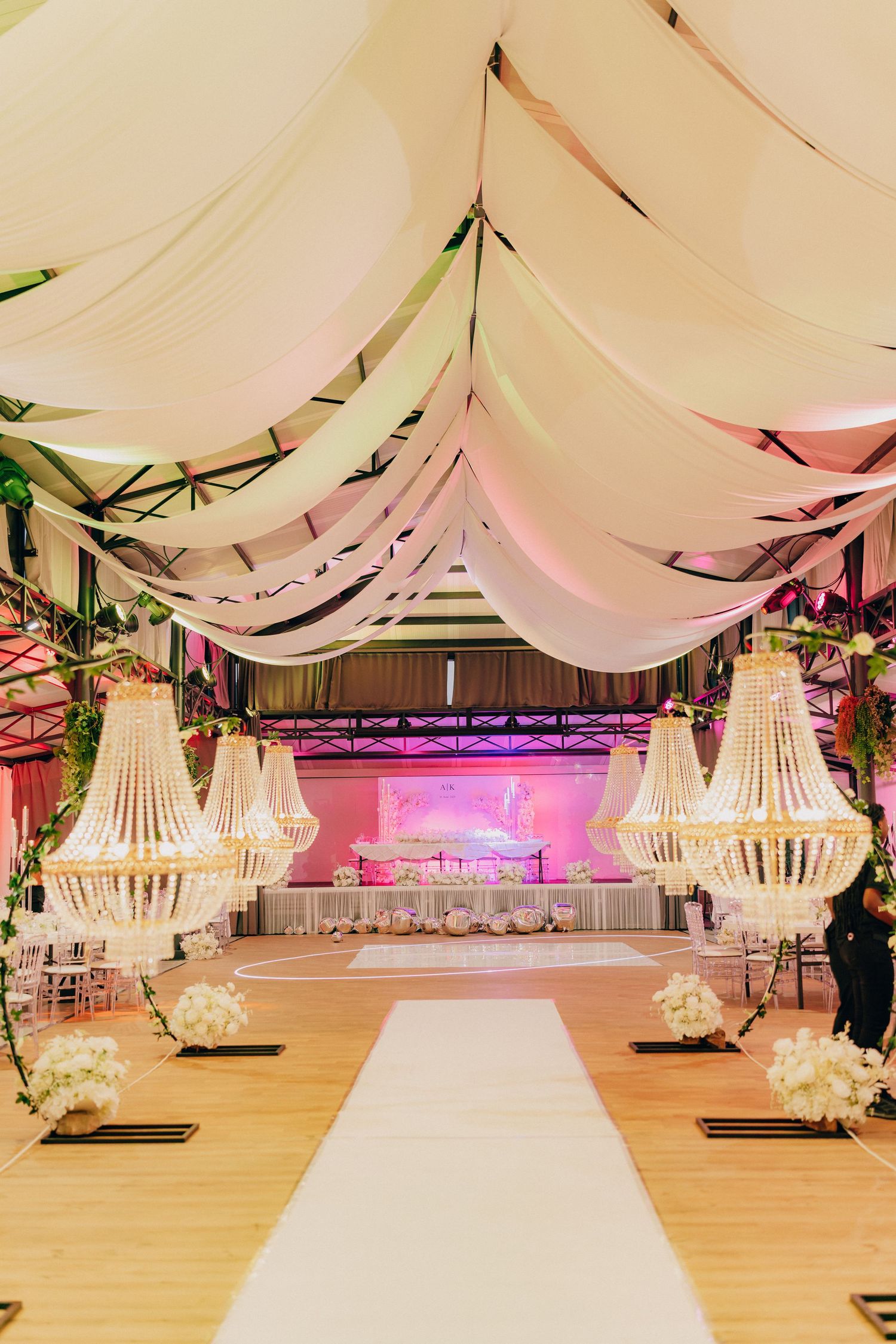 Elegant wedding reception venue with draped white fabric ceiling and illuminated chandeliers on a wooden dance floor.