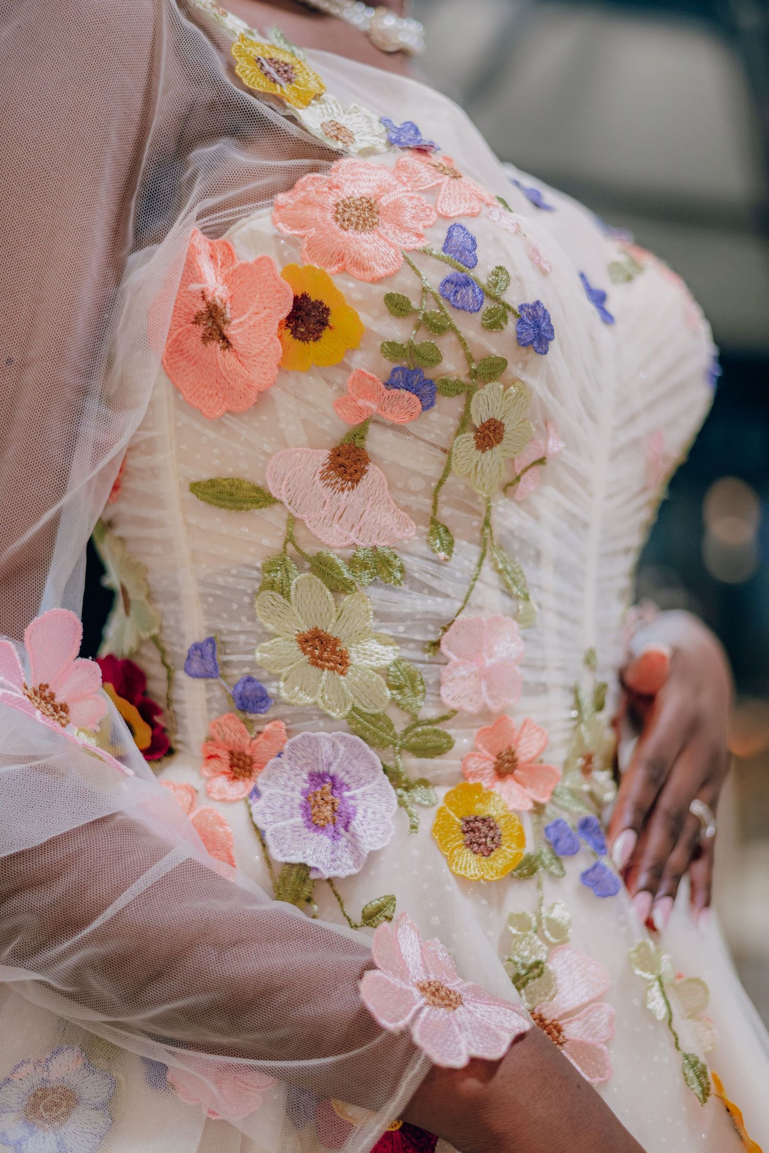 Close-up detail of a wedding dress bodice featuring delicate embroidered flowers in pink, yellow and purple on white tulle fabric.