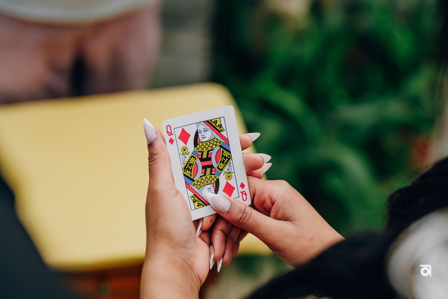 Close-up view of hands holding a playing card showing a Queen of Hearts against a blurred background.