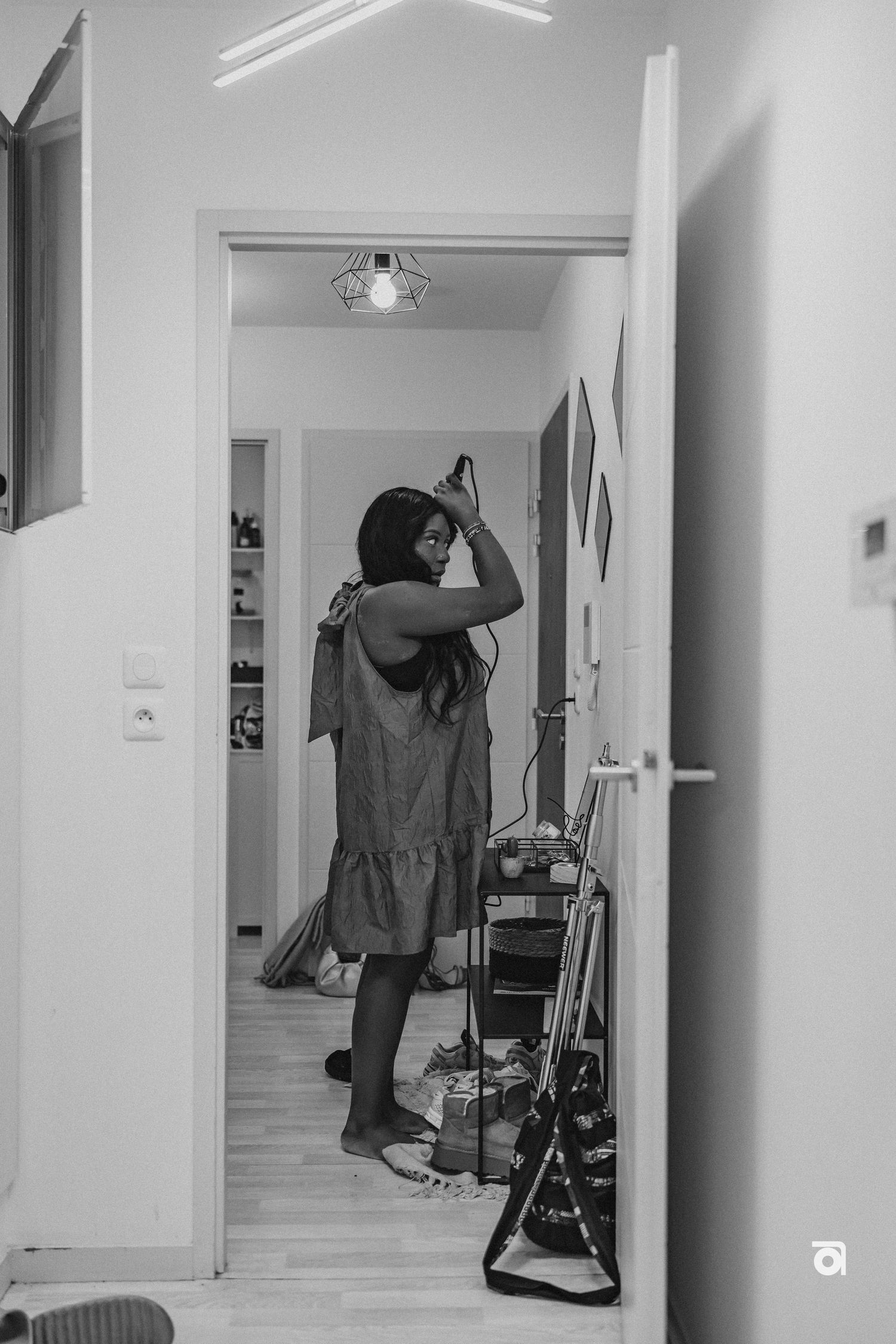 Black and white photo showing a person in a loose dress adjusting their hair in front of a mirror.