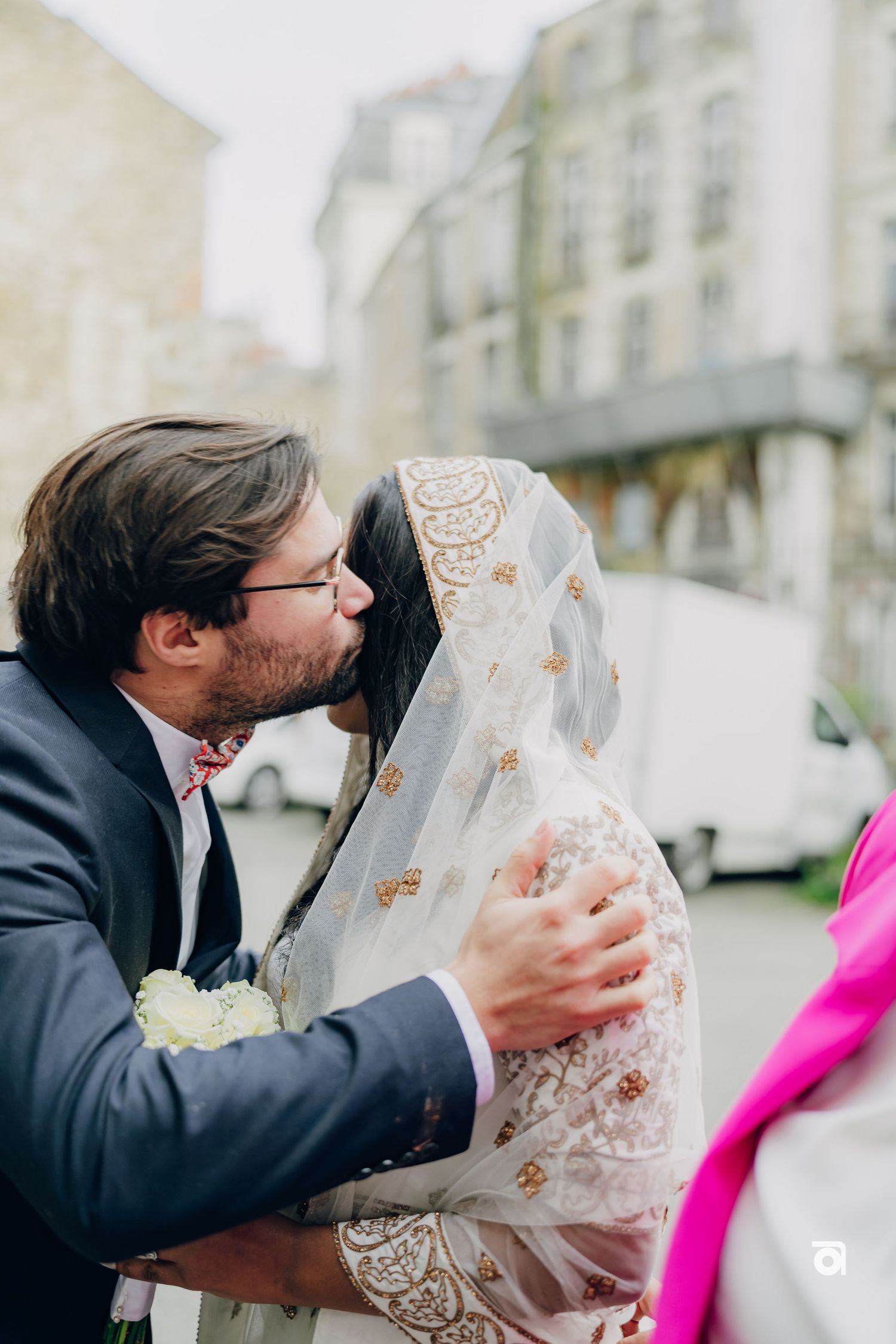 A wedding couple shares an intimate moment outdoors with the bride wearing an ornate lace veil.