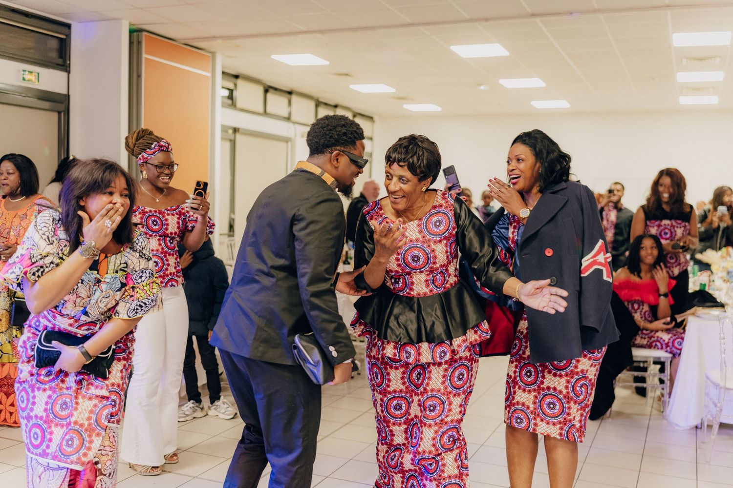 People dancing together at a celebration wearing colorful traditional African print dresses.