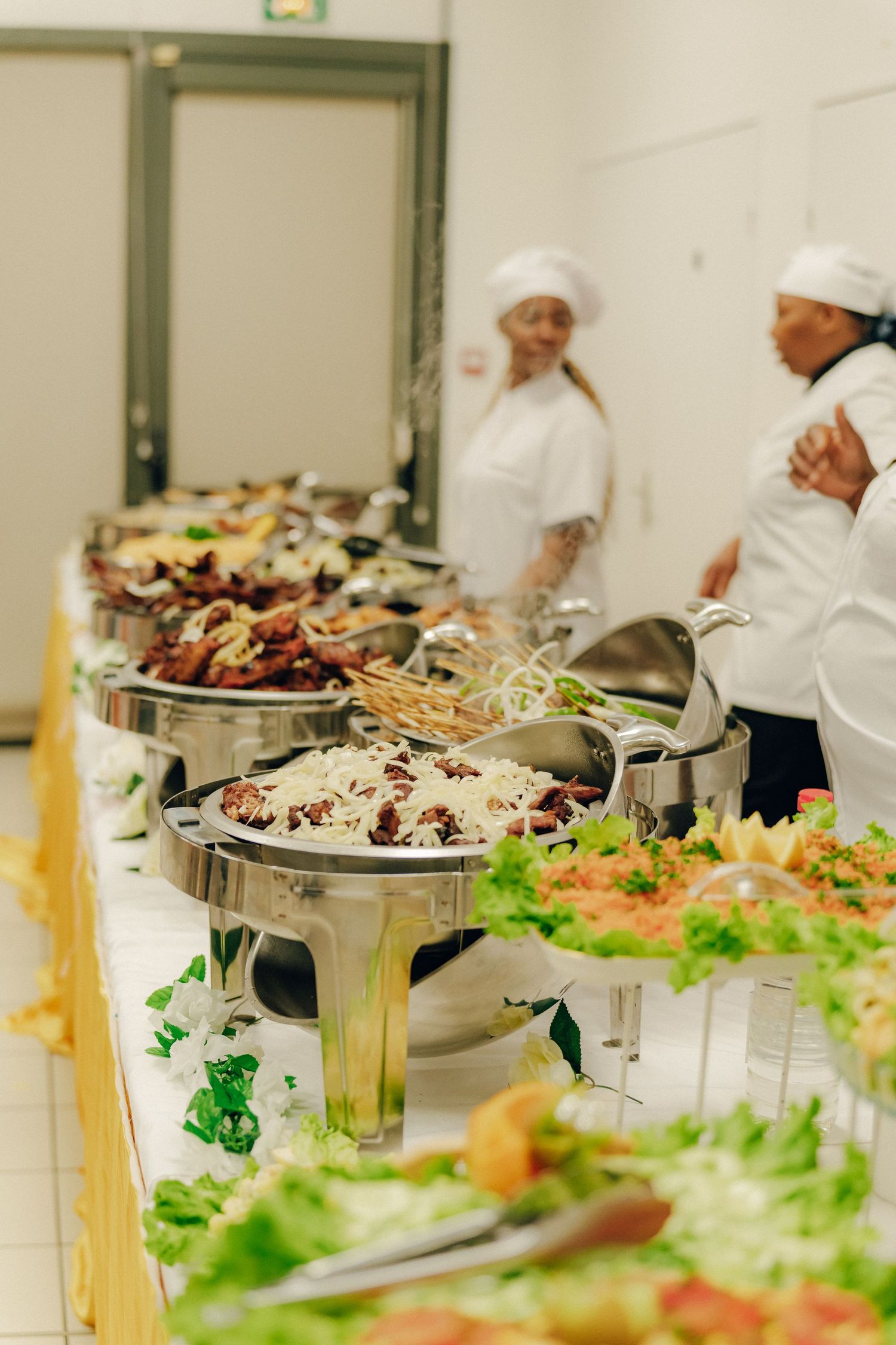 Catering staff in white uniforms standing behind a buffet line with various dishes.
