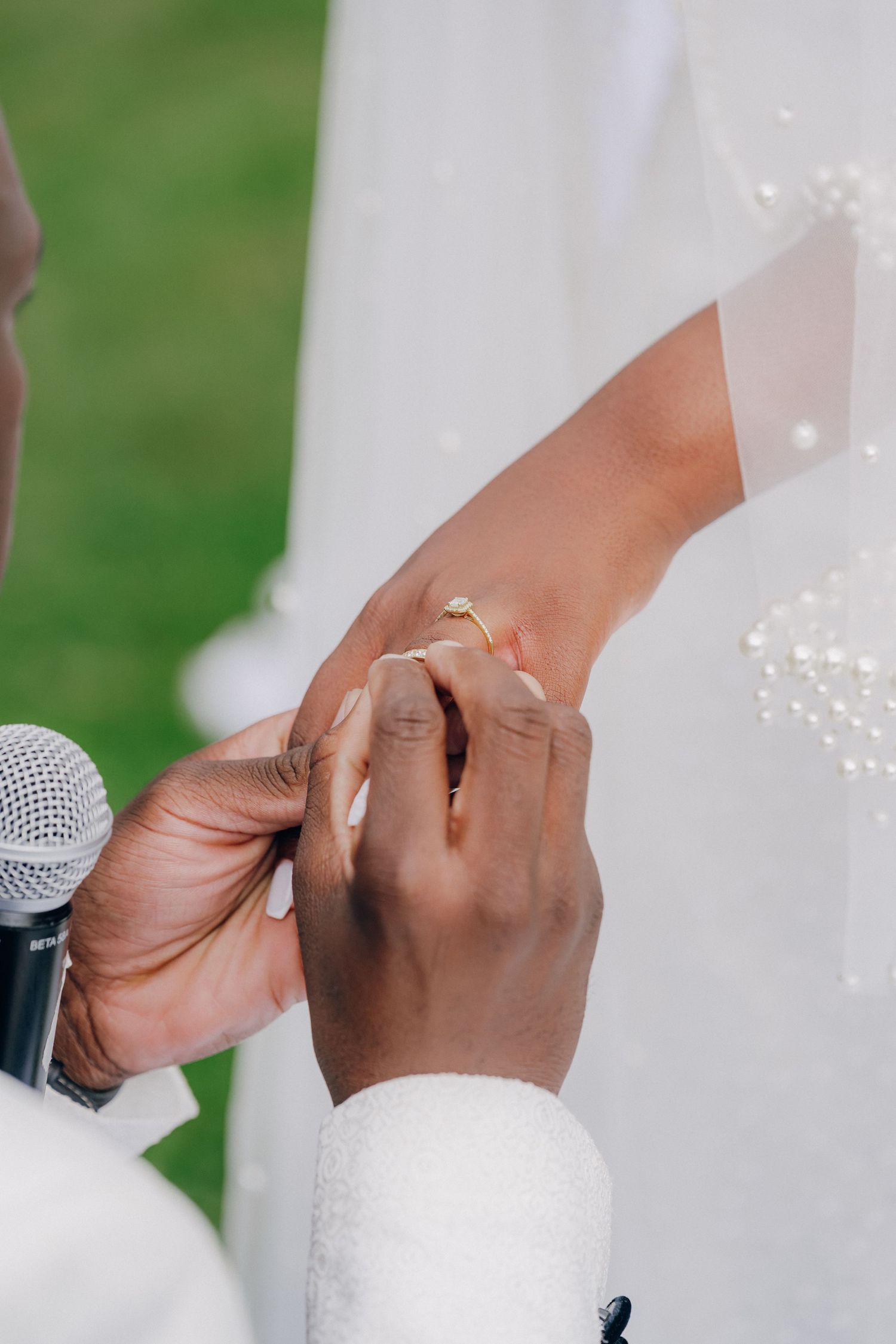 Close-up of hands exchanging rings during a wedding ceremony with a microphone visible.