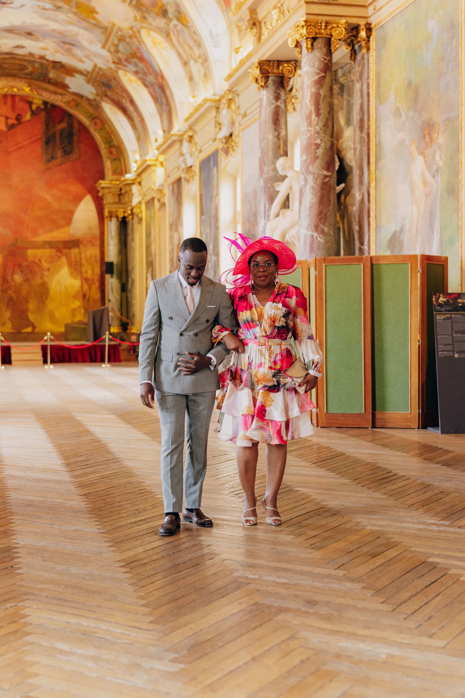 Couple poses in an ornate palace hallway with classical architecture and painted ceilings.
