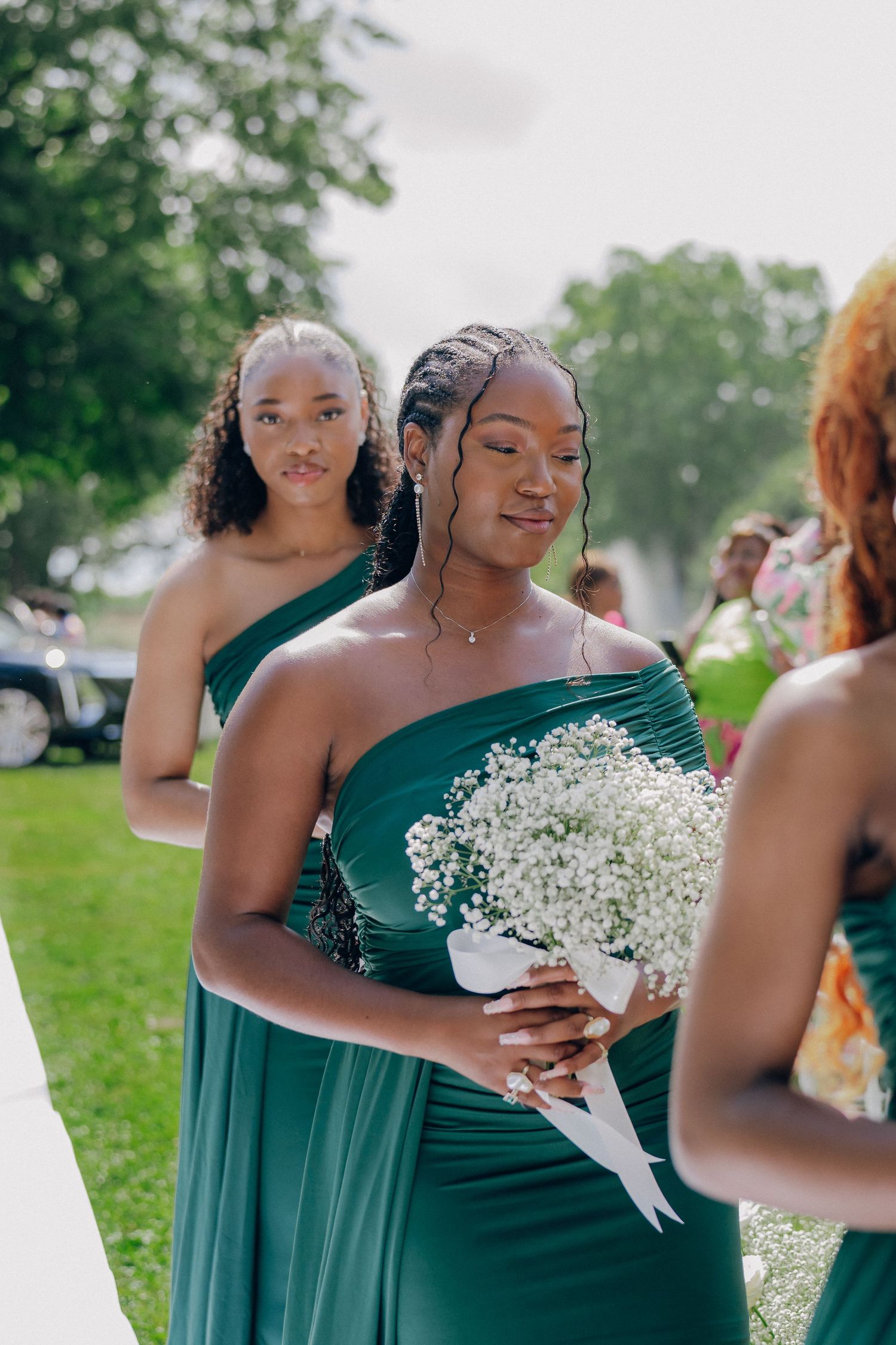 Bridesmaids in matching green off-shoulder dresses holding delicate white bouquets during ceremony.