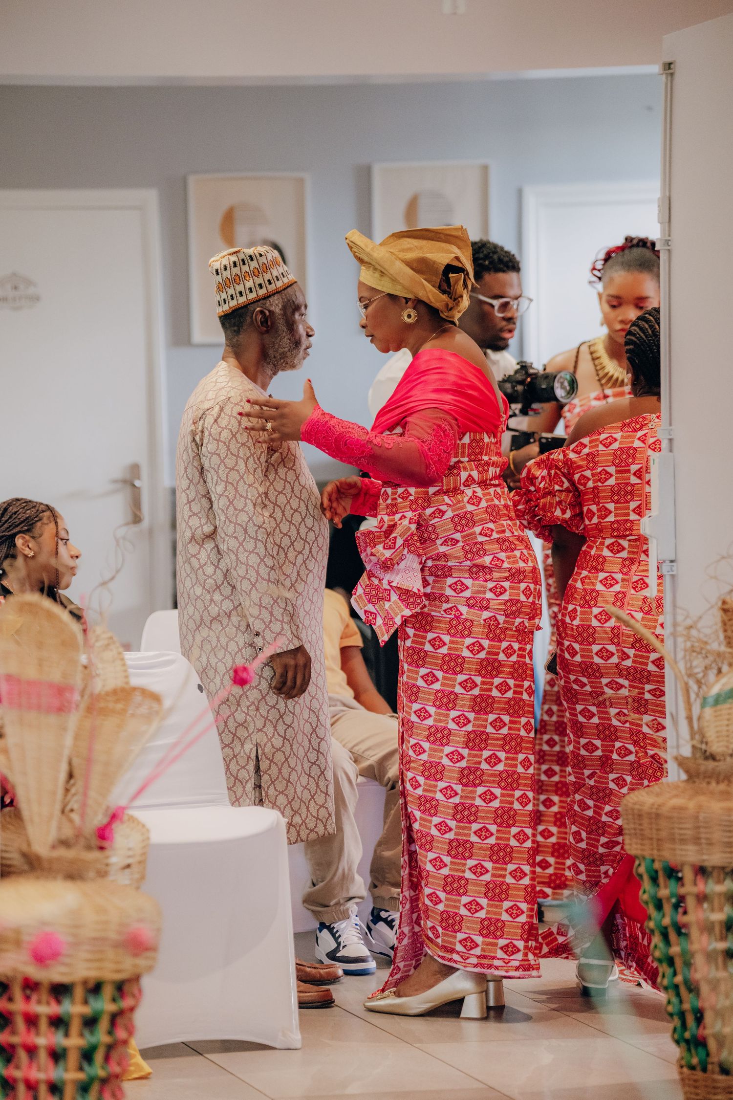 Traditional wedding celebration with guests in red and cream patterned attire dancing together.