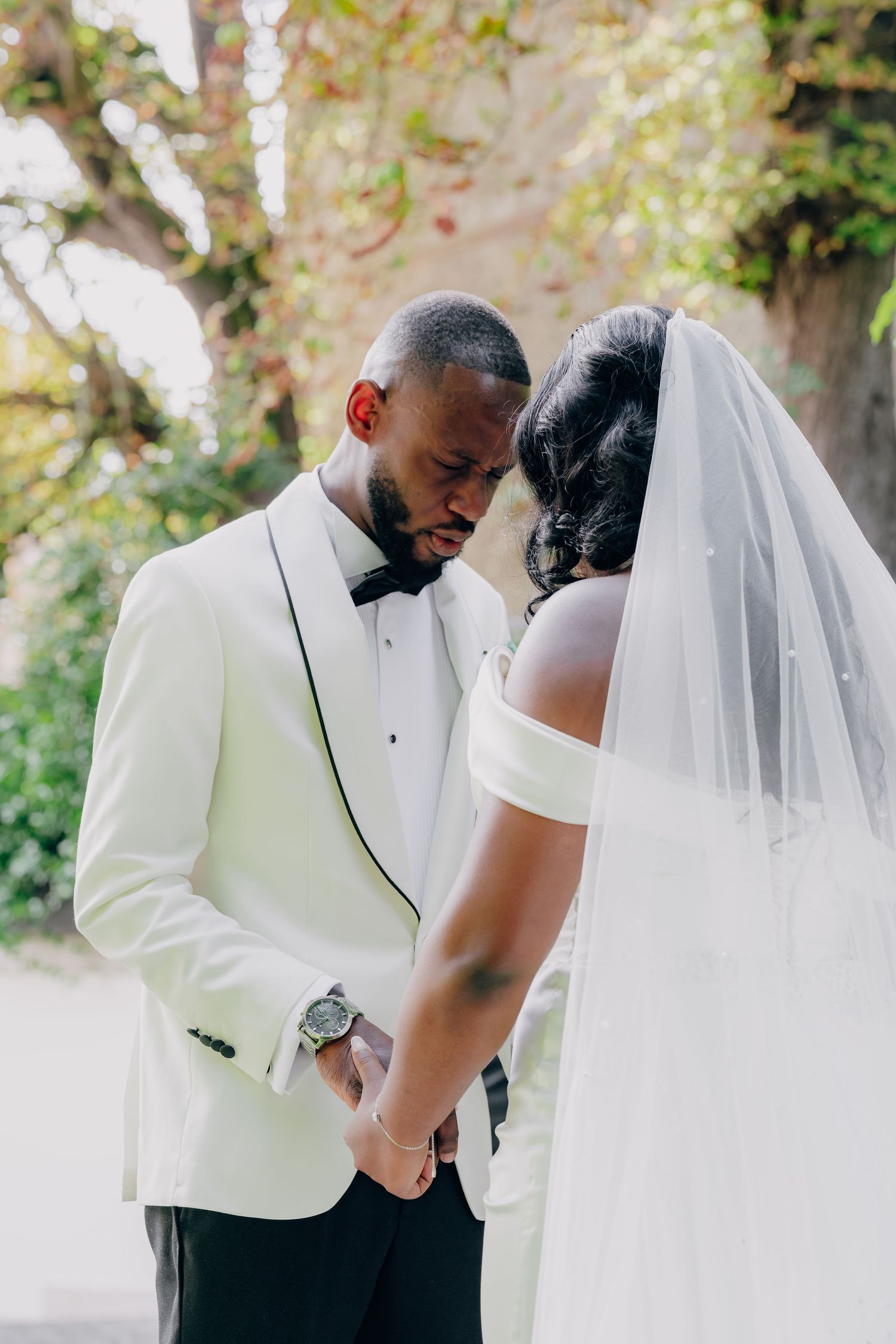 A tender wedding moment shared between newlyweds under trees with soft natural lighting.