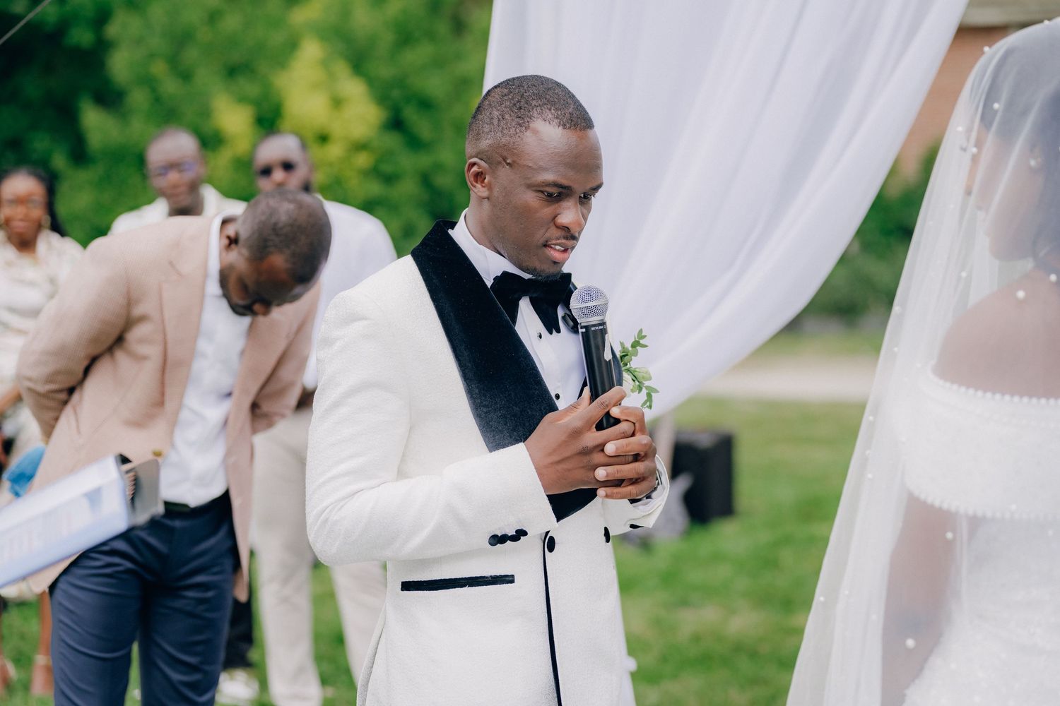 Outdoor wedding ceremony with white drapery and guests in formal attire.