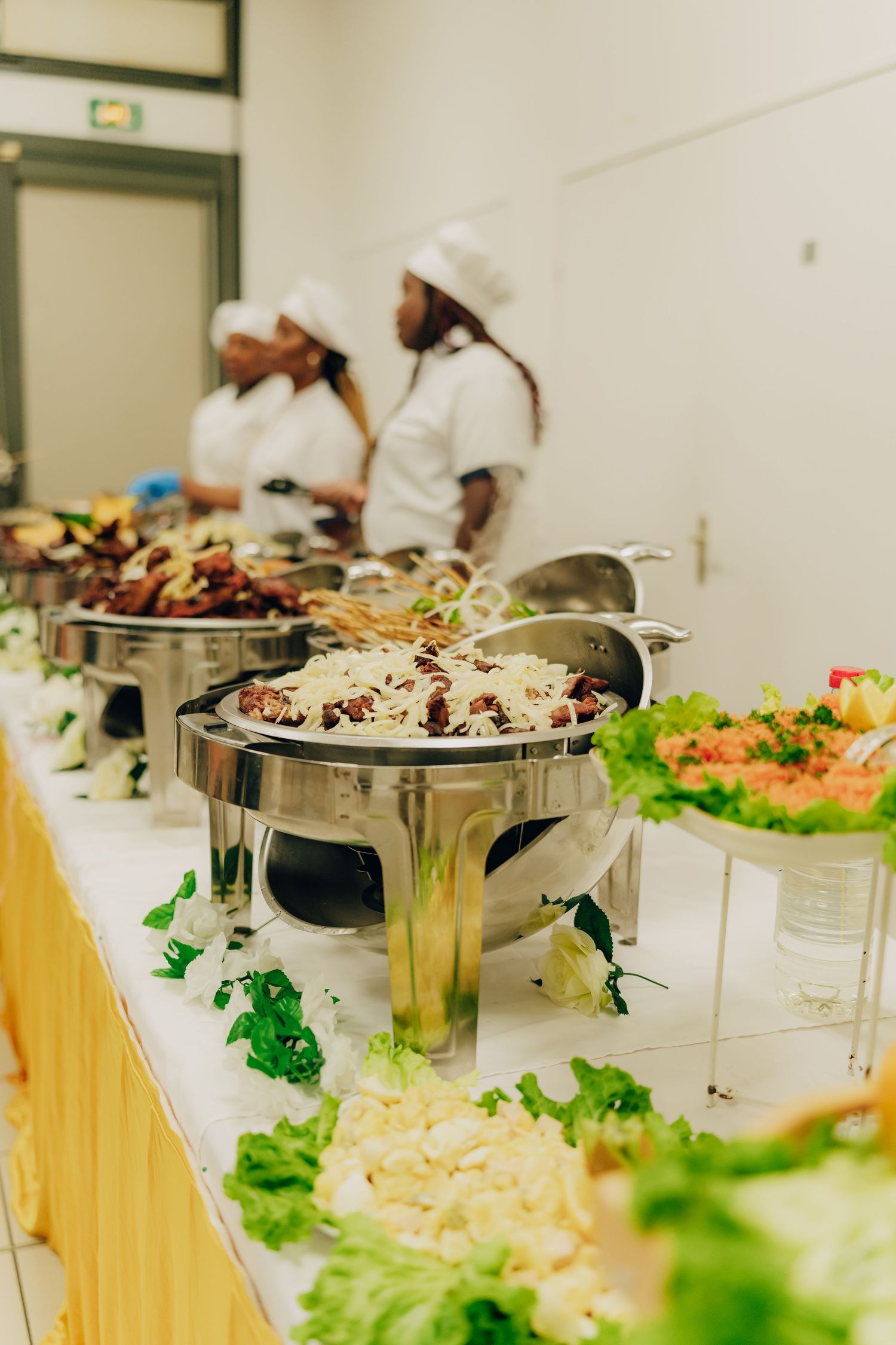 Buffet setup with chafing dishes and fresh vegetables displayed on a white table.