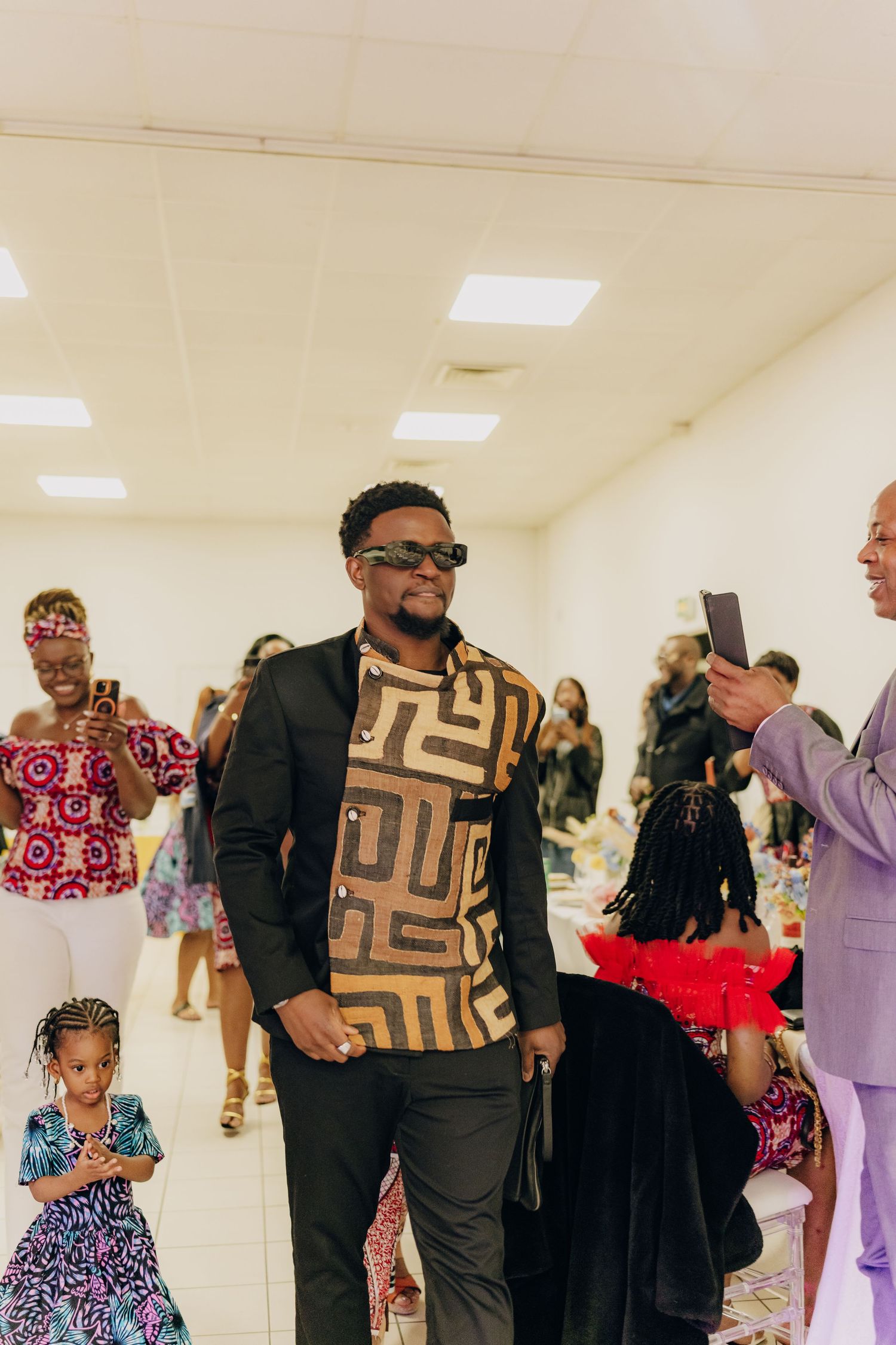 Fashionable attendee in geometric print shirt and blazer smiles at indoor event.