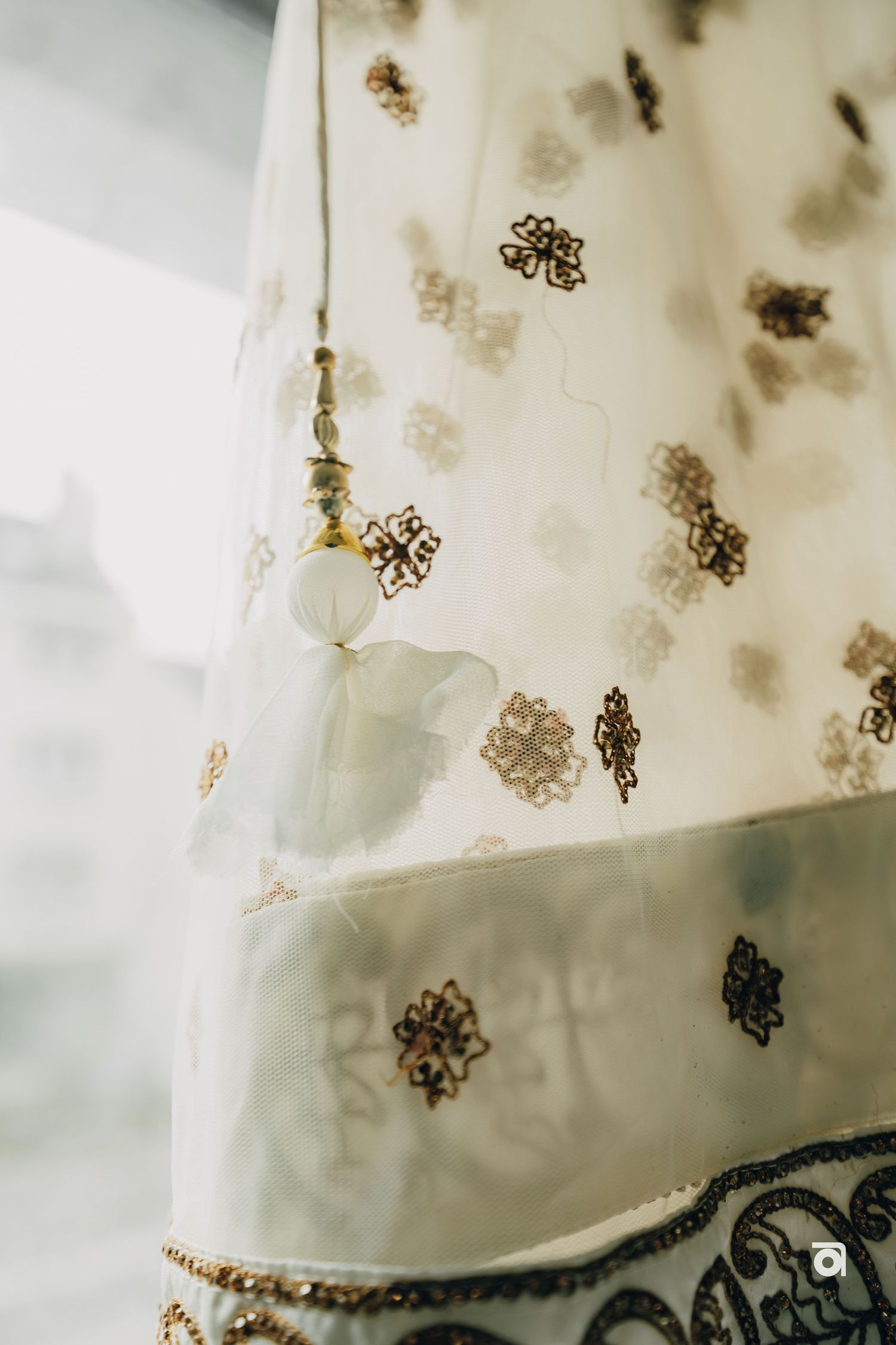 Close-up detail of delicate gold floral embroidery pattern on sheer white fabric with soft natural lighting.