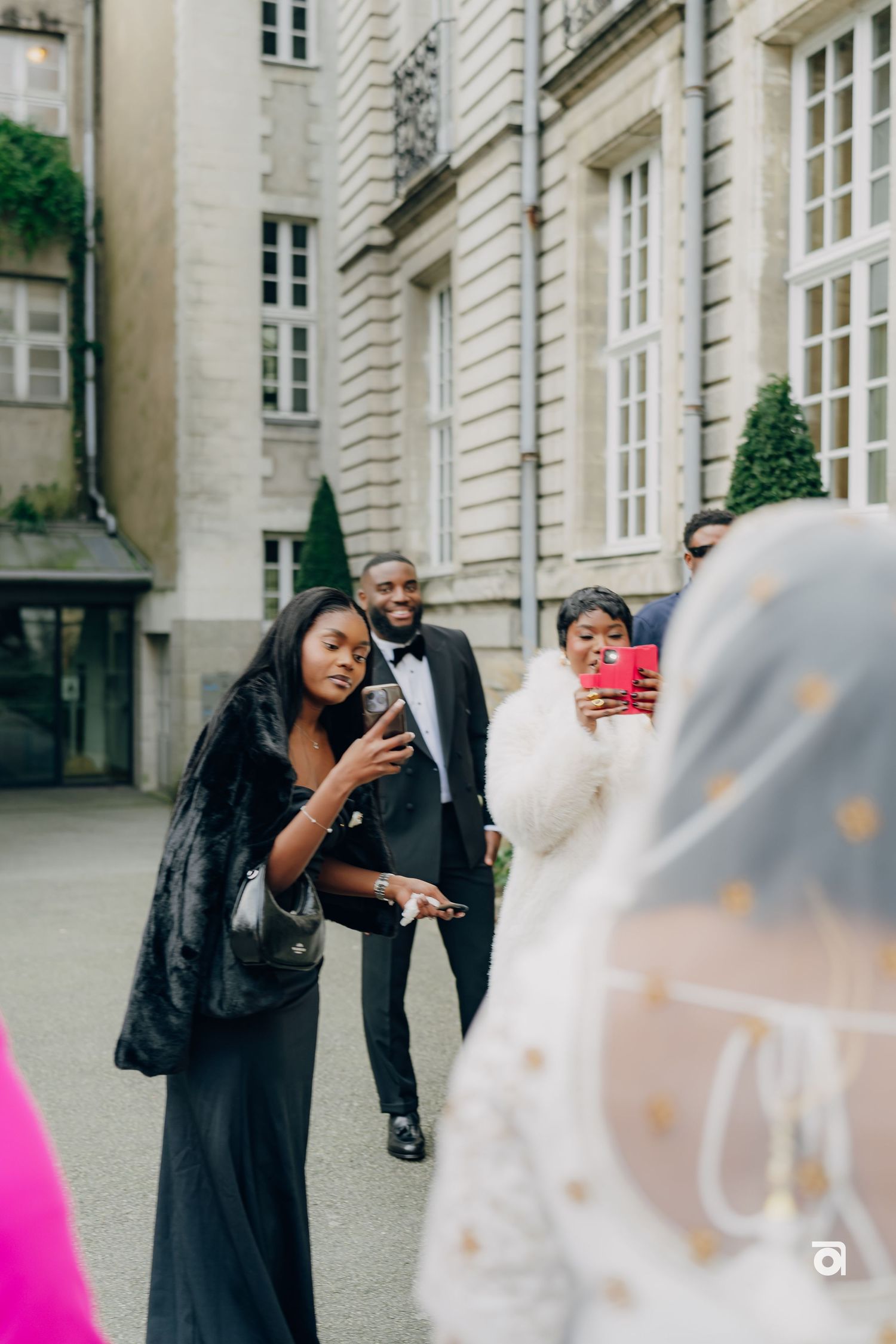 Wedding guests taking photos outside an elegant stone building with decorative architecture.