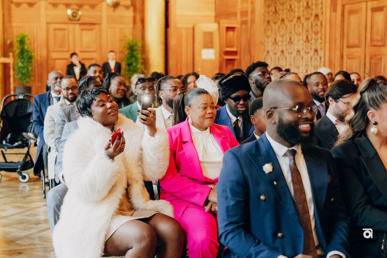 Wedding guests smile and laugh during a joyful indoor ceremony in an elegant room with ornate walls.