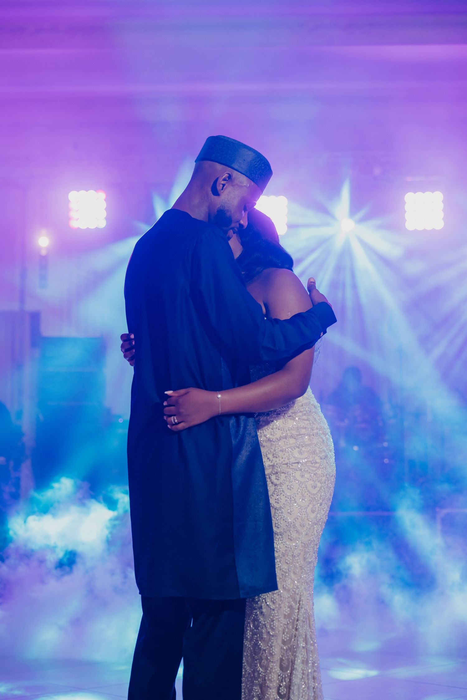 A couple shares a romantic dance on a misty dance floor illuminated by purple and blue lighting effects.