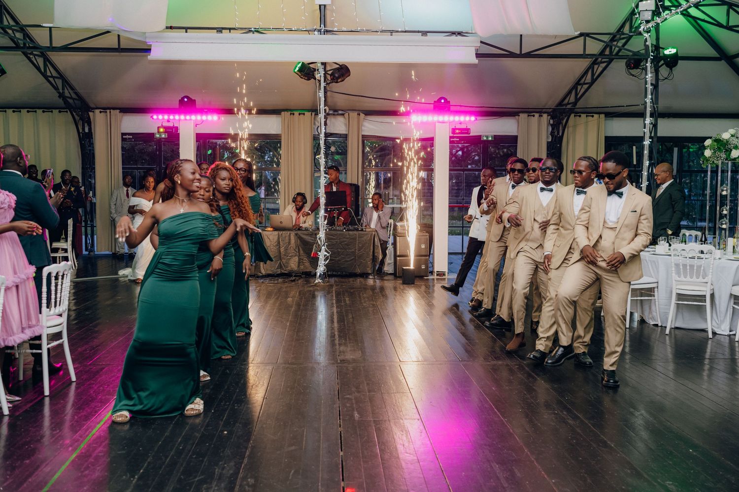 Wedding reception dance floor filled with guests in formal attire dancing under colorful lighting.