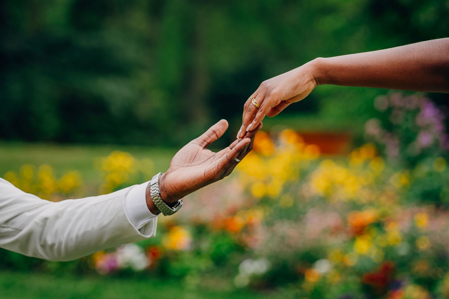 Two hands reaching towards each other in a garden with colorful blurred flowers in the background.
