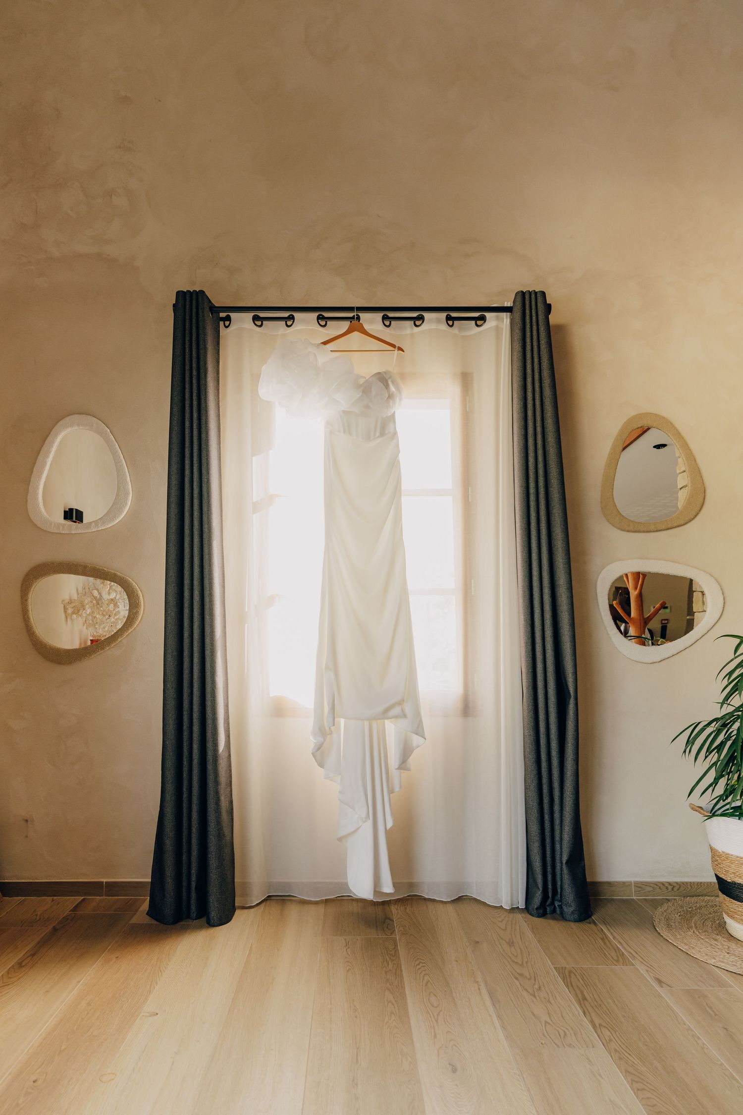 White robes hang elegantly against a beige wall with round mirrors and dark curtains in a minimalist dressing room.