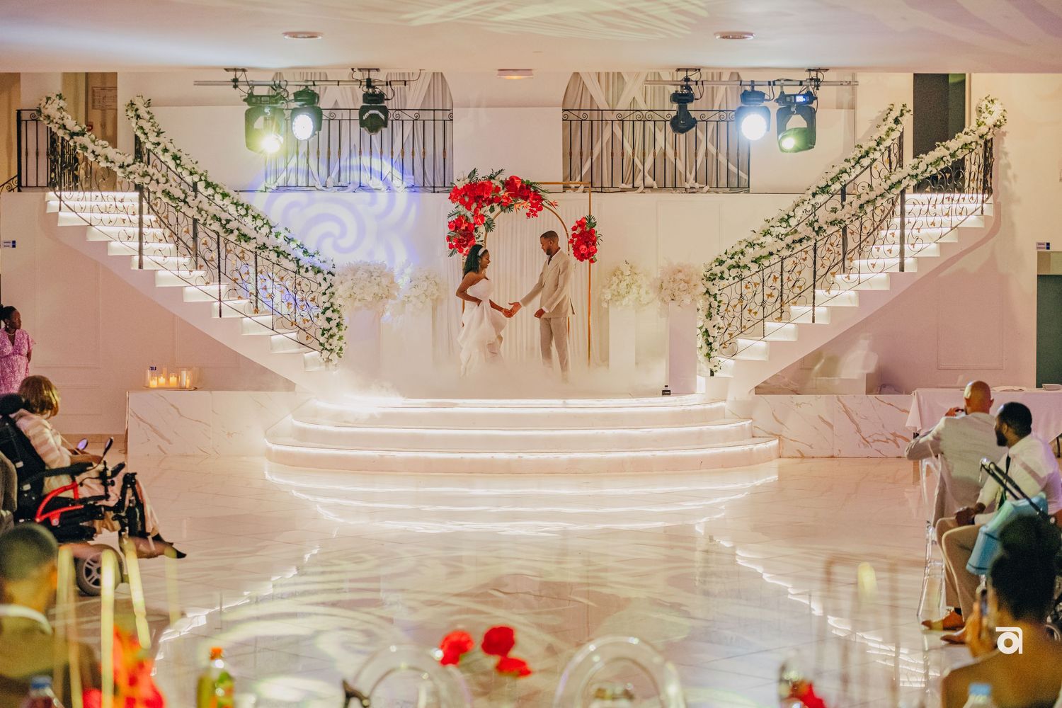 Elegant grand staircase at wedding venue decorated with red roses, glowing steps, and ornate railings in white decor.