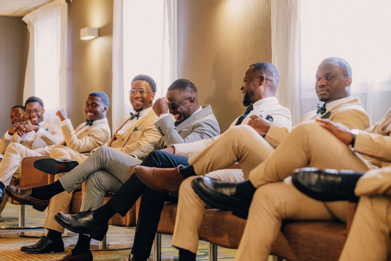 A group of men in matching khaki pants sit together in chairs laughing during a social gathering.