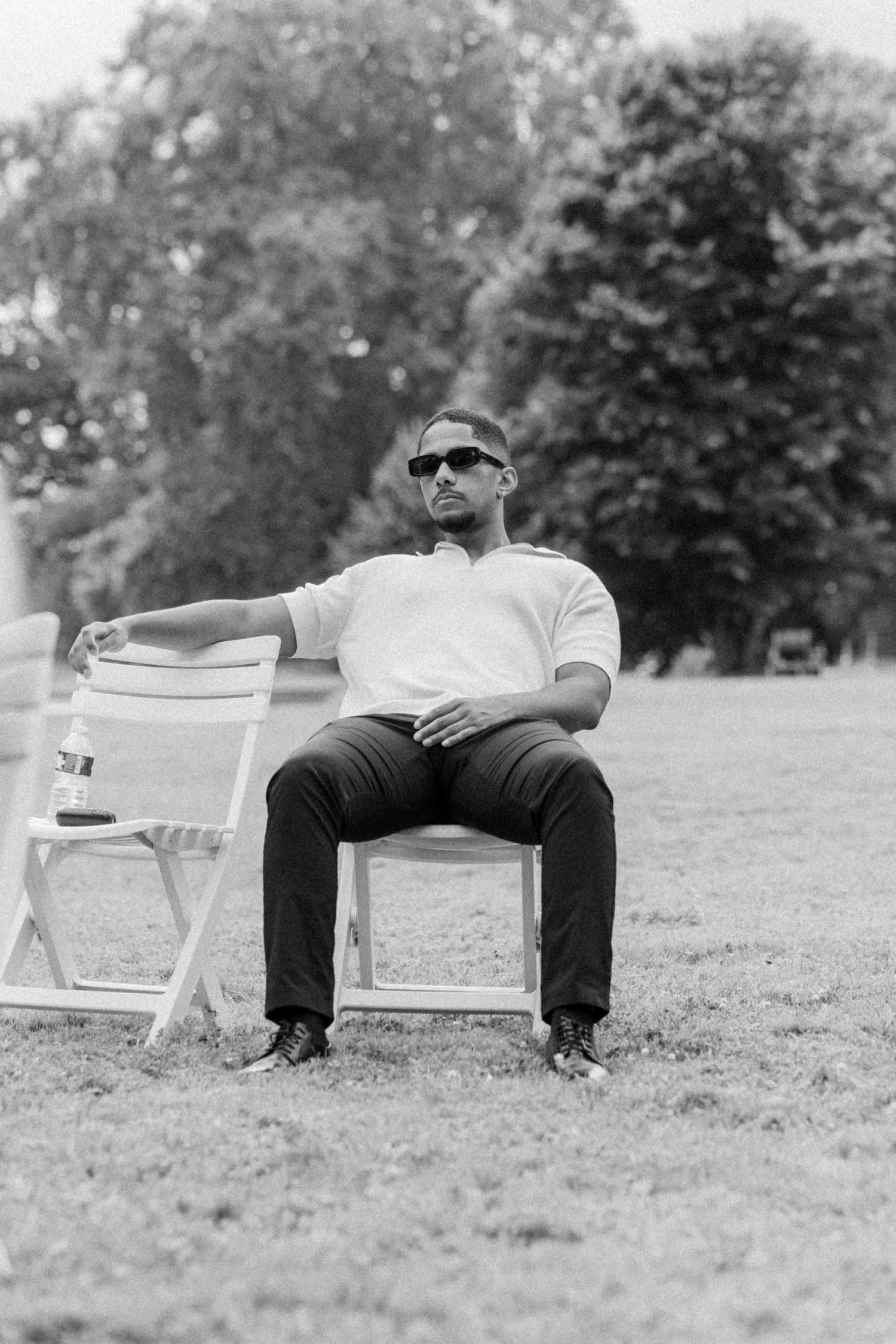 Black and white photo of empty white chairs arranged on grass at an outdoor venue.