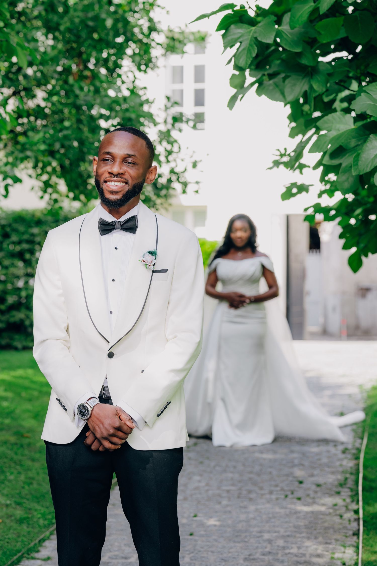 Wedding photos in a garden setting with white tuxedo jackets and formal attire against lush greenery.