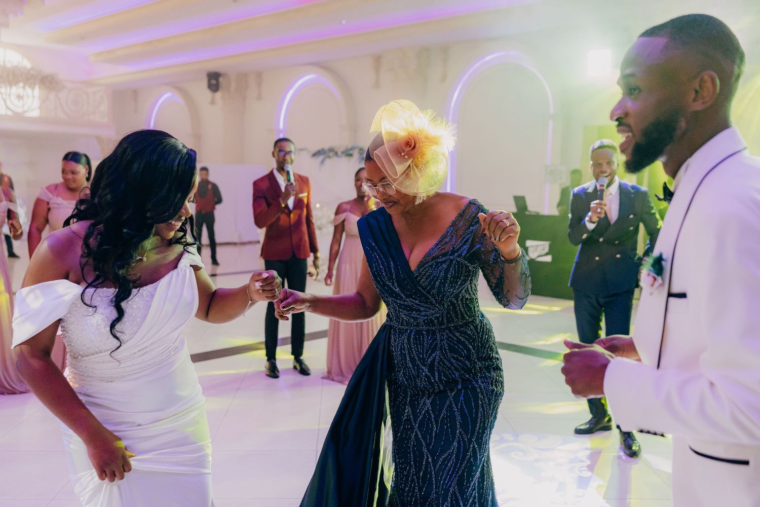 Wedding guests dance together on an illuminated dance floor with purple ambient lighting in an elegant venue.