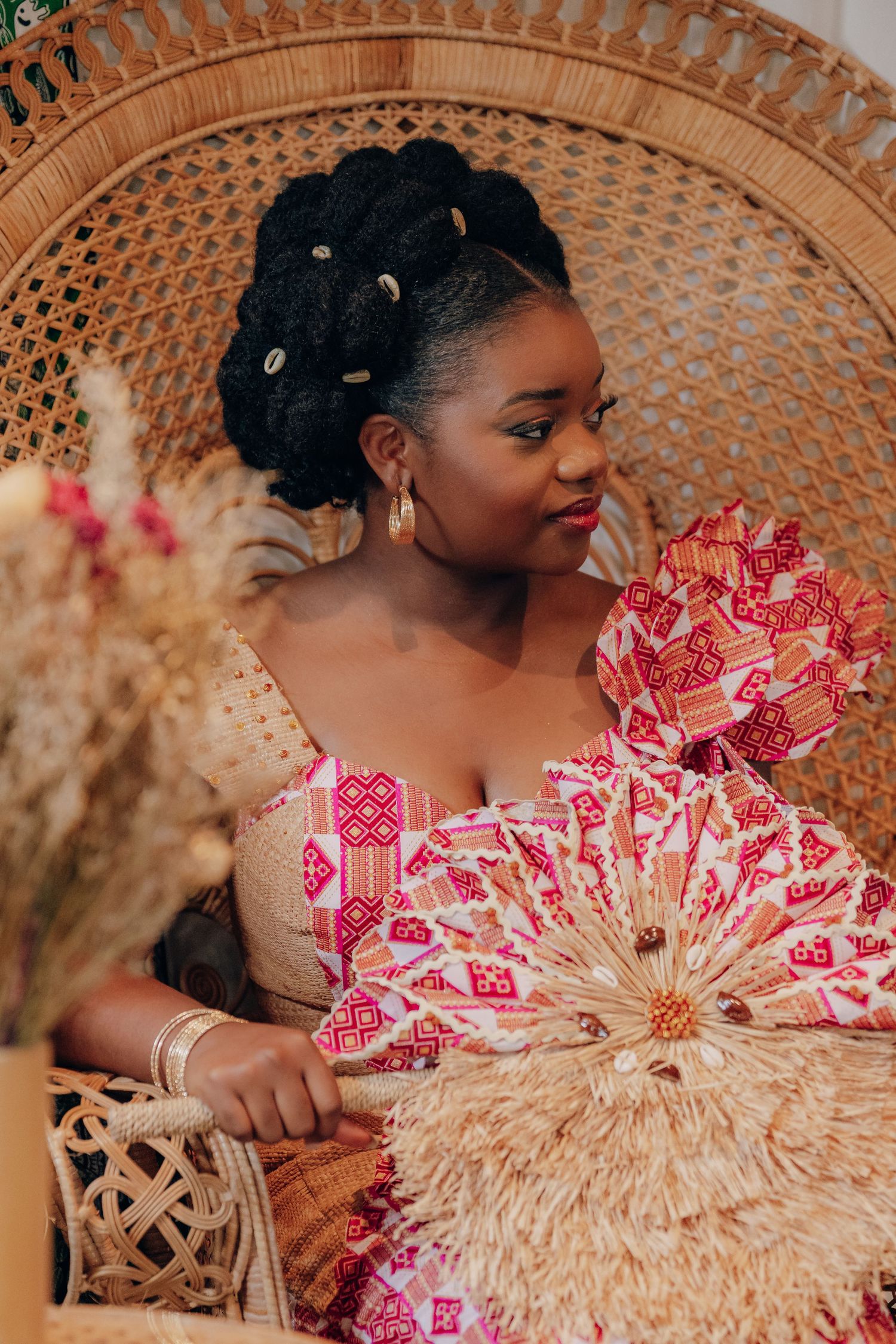 A decorative peacock chair setting with pink and red floral accents against a woven rattan backdrop.