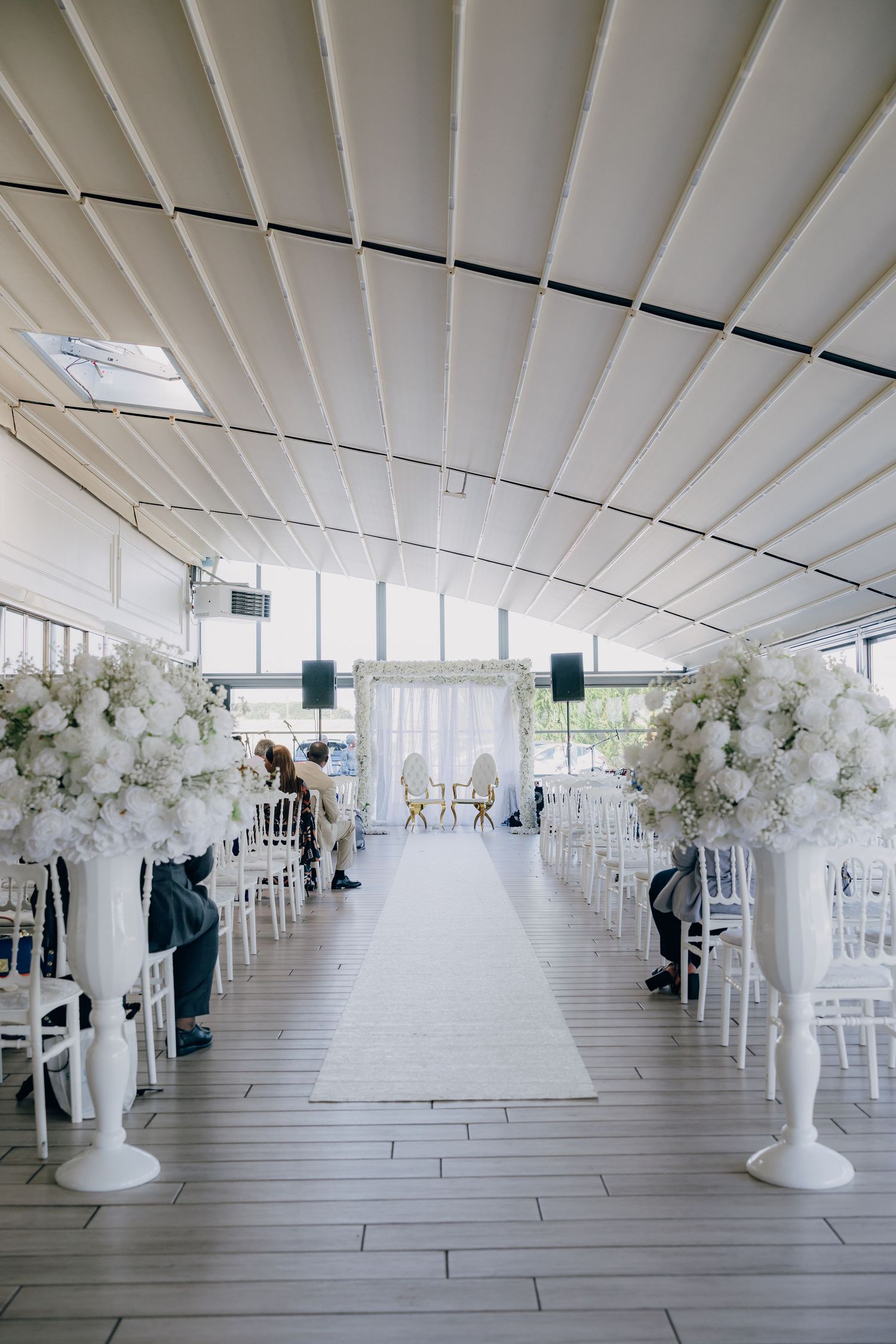 White floral arrangements line an elegant indoor venue with floor-to-ceiling windows and modern white decor.