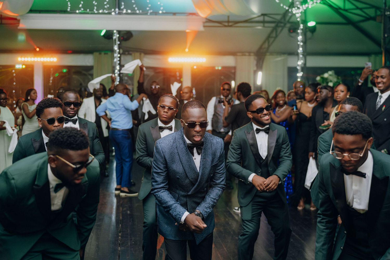 Groomsmen performing a synchronized dance routine at a wedding reception in formal attire.