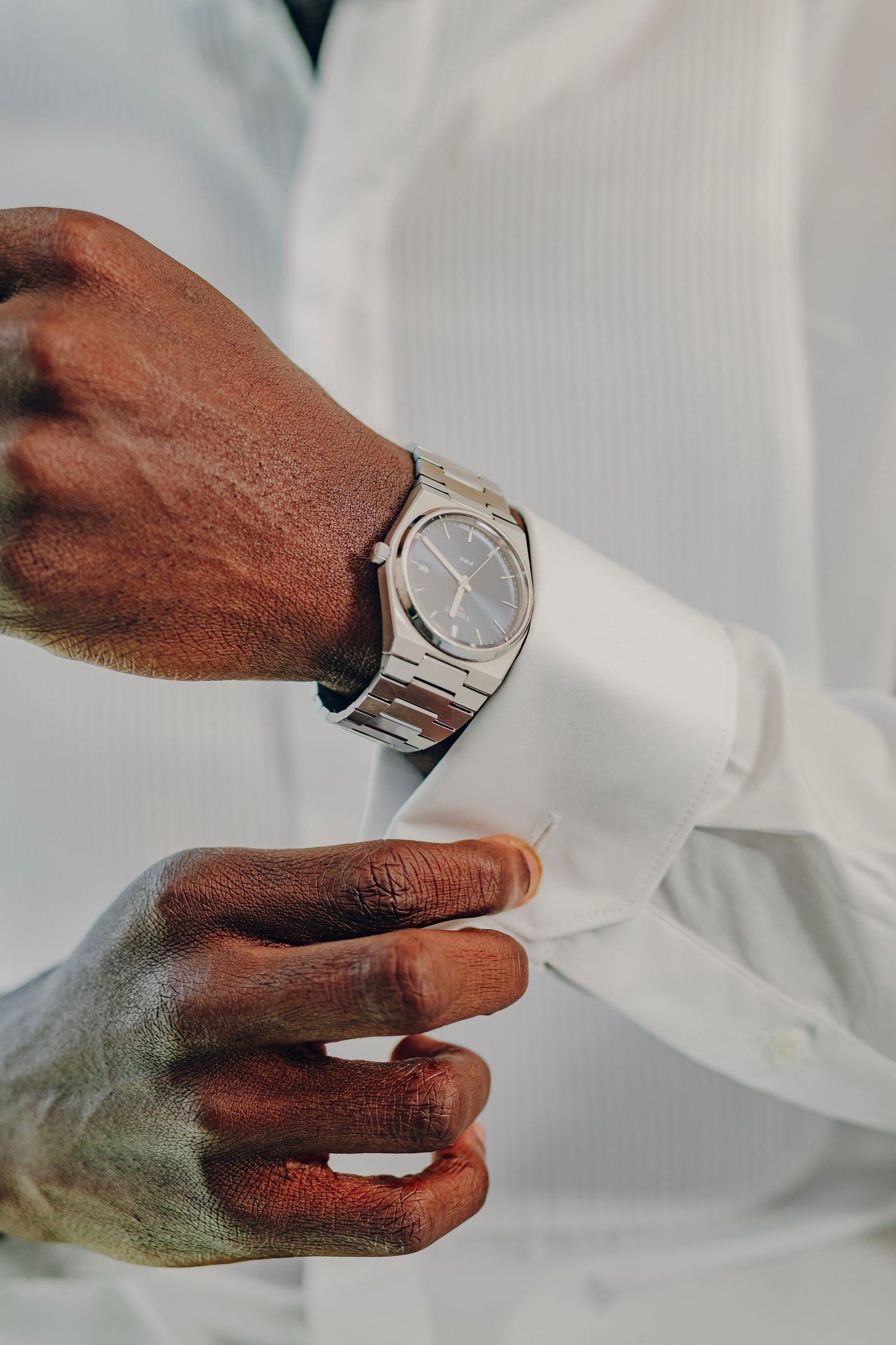 Detail shot of silver luxury watch on wrist with white dress shirt cuff.