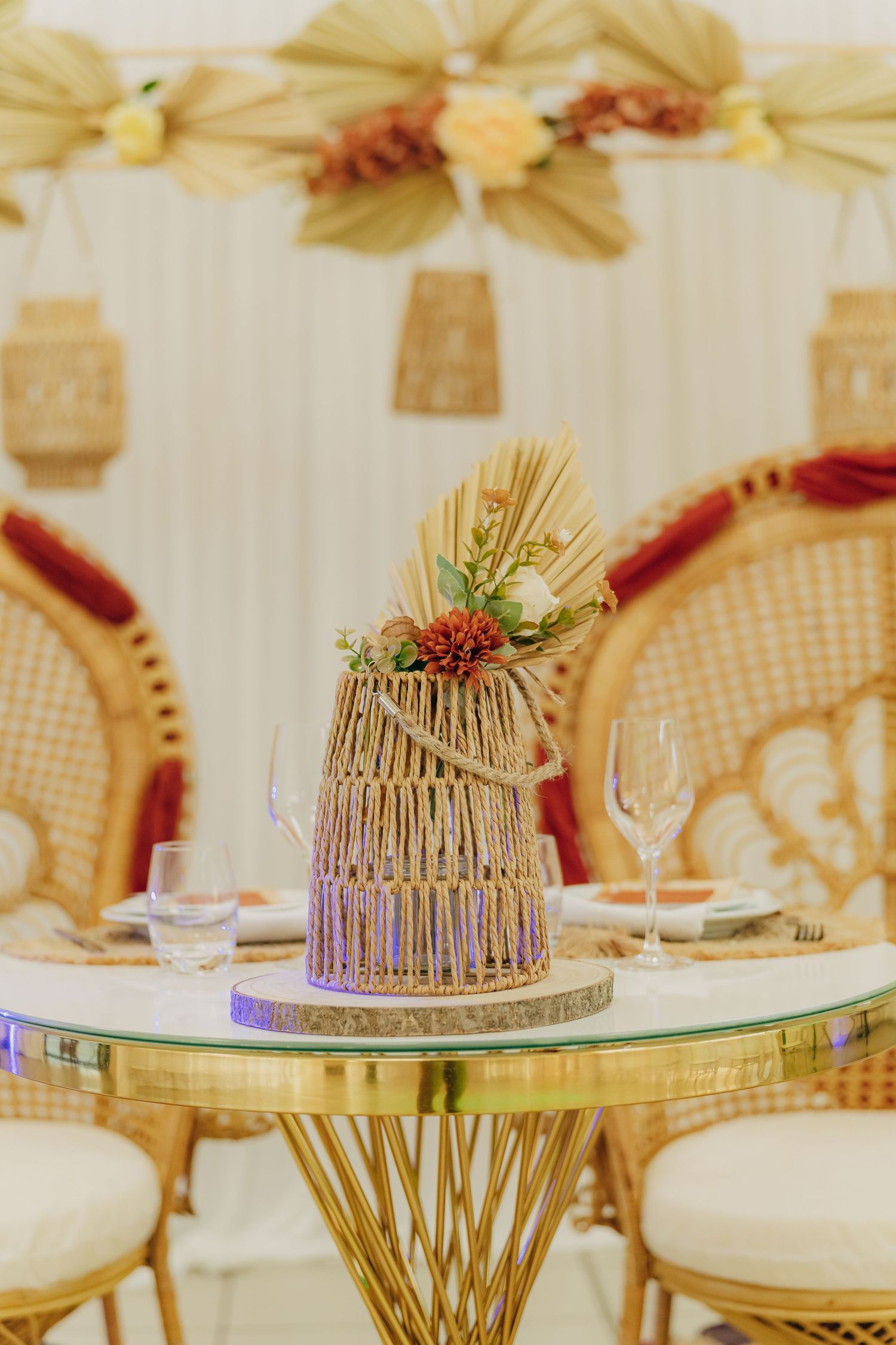A rustic woven centerpiece with wheat stalks and berries sits on a round glass table with cane dining chairs.