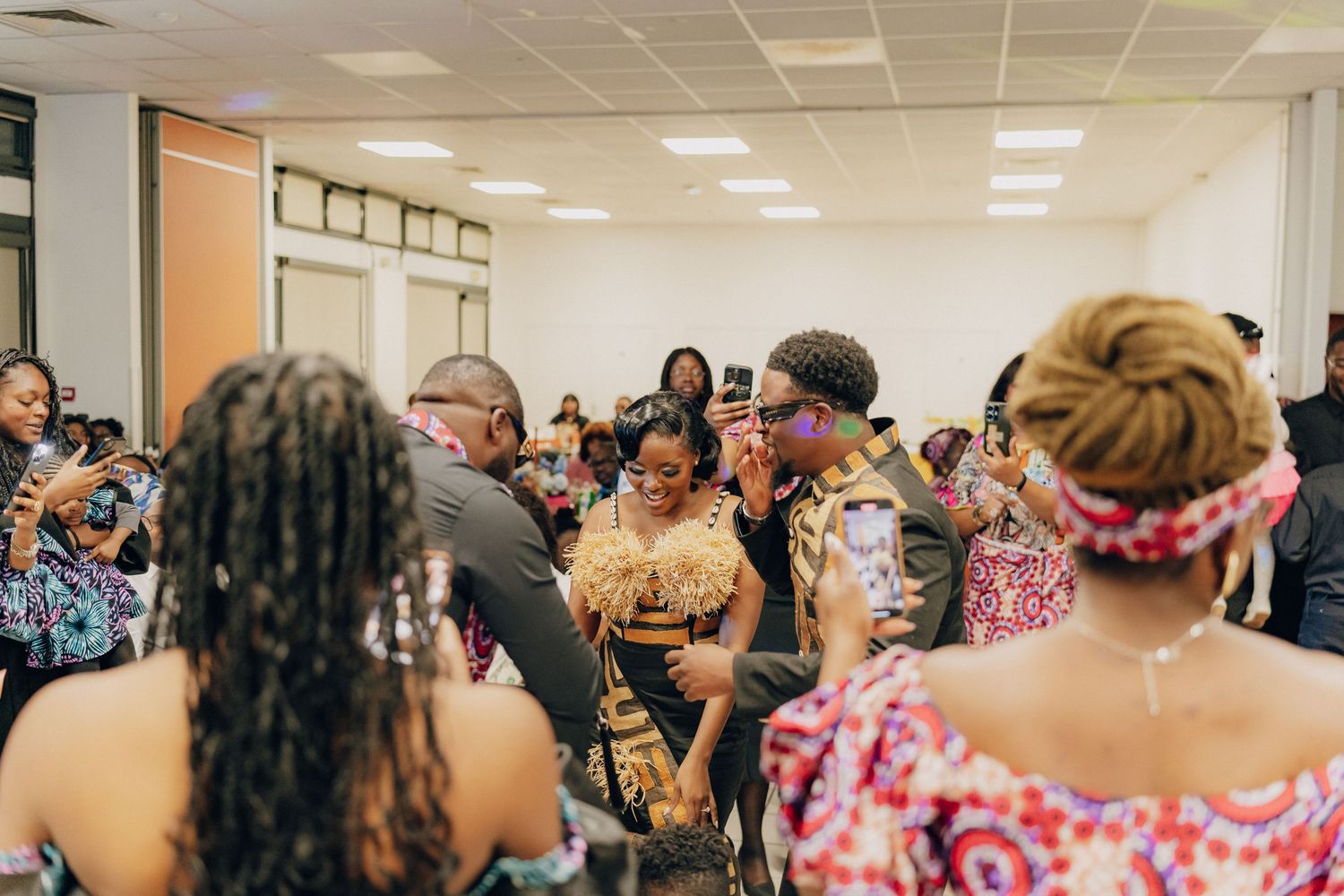 A crowd of people seated and socializing at an indoor event wearing colorful patterned clothing.